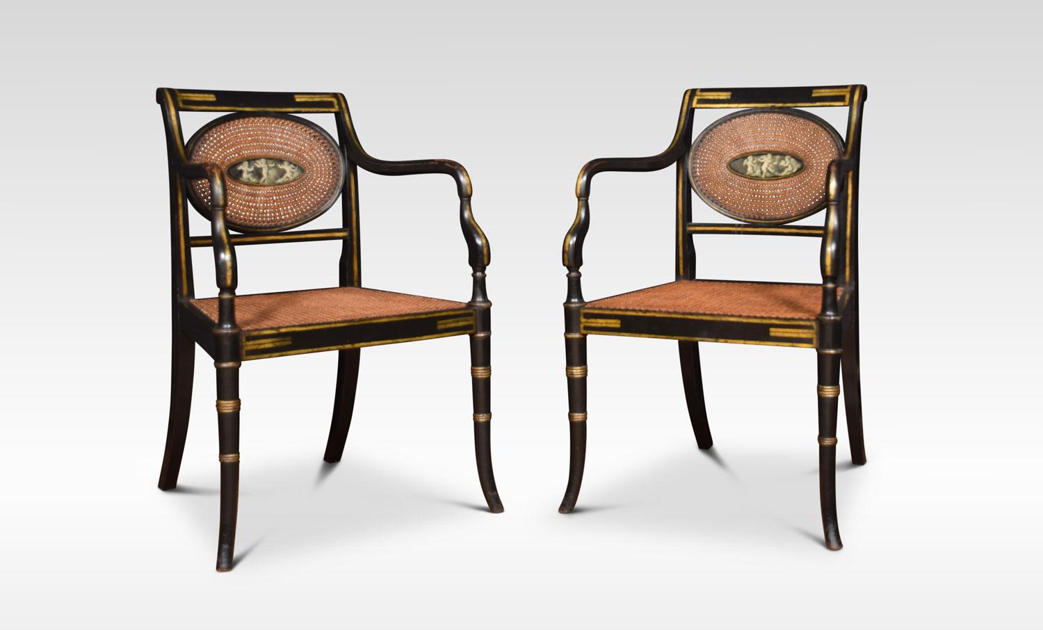 Refined set of eight English Regency style cane armchairs, Classic in form with an ebonized finish and original gold painted details. The backrest with central oval painting depicting three cherubs, each chair has a different design. Above cane work