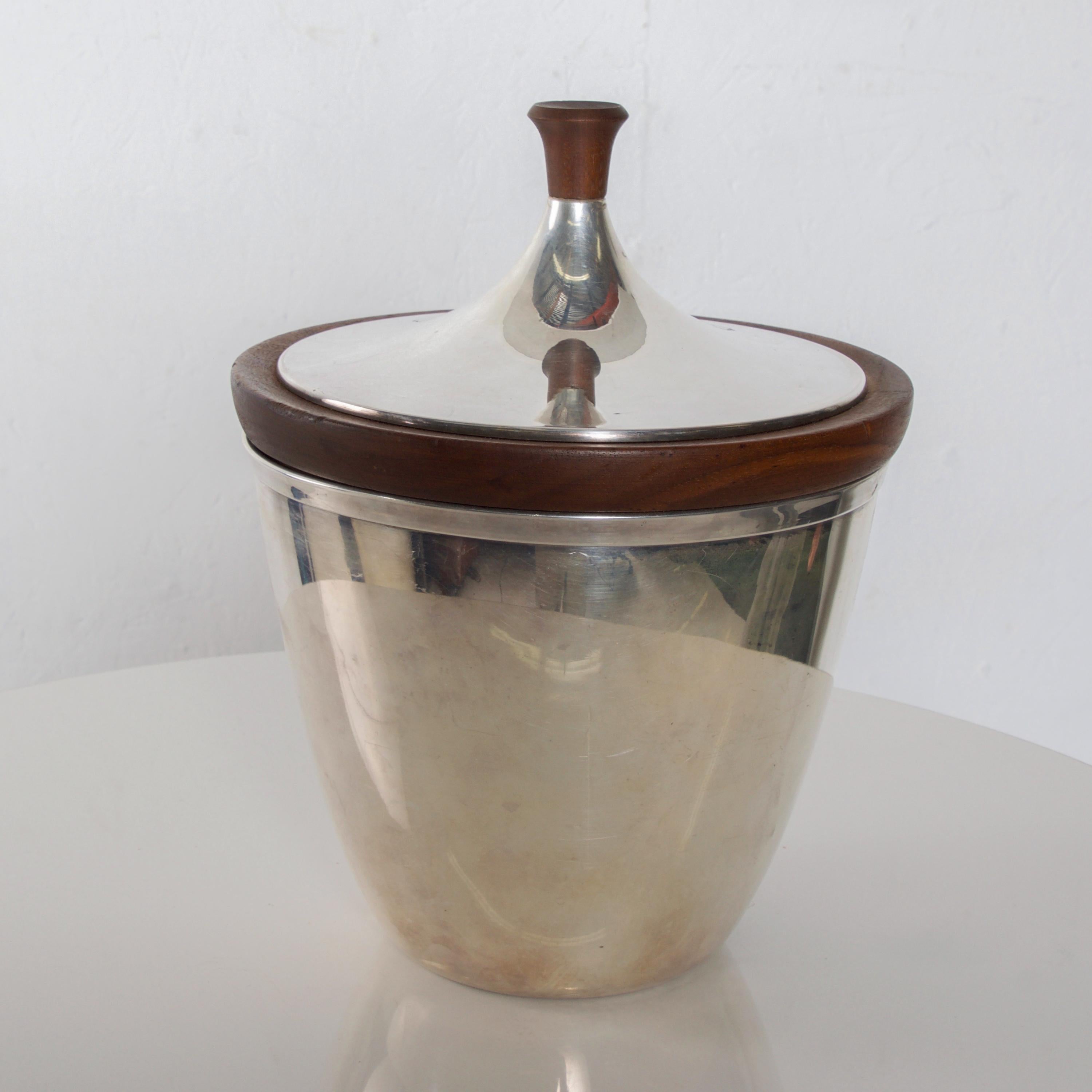 Mid-Century Modern International silver plated and aluminum ice bucket trimmed in walnut wood.
Stamped on bottom. Difficult to read.
Measures: 10 1/2 height x 9 inches diameter, 6 1/2 height without lid. Interior (ice area) 6 H x 7 1/2 inches
