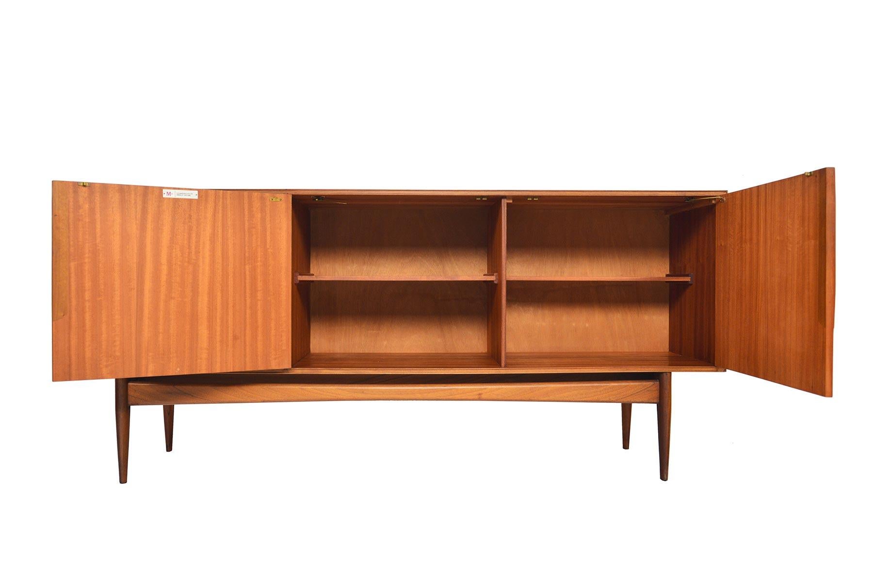 This Mid-Century Modern atomic low line teak sideboard was manufactured by A.H. McIntosh in the 1960s. A bank of three drawers sit to the left of two bay interior with fixed shelves. Recently refinished and in excellent condition.
