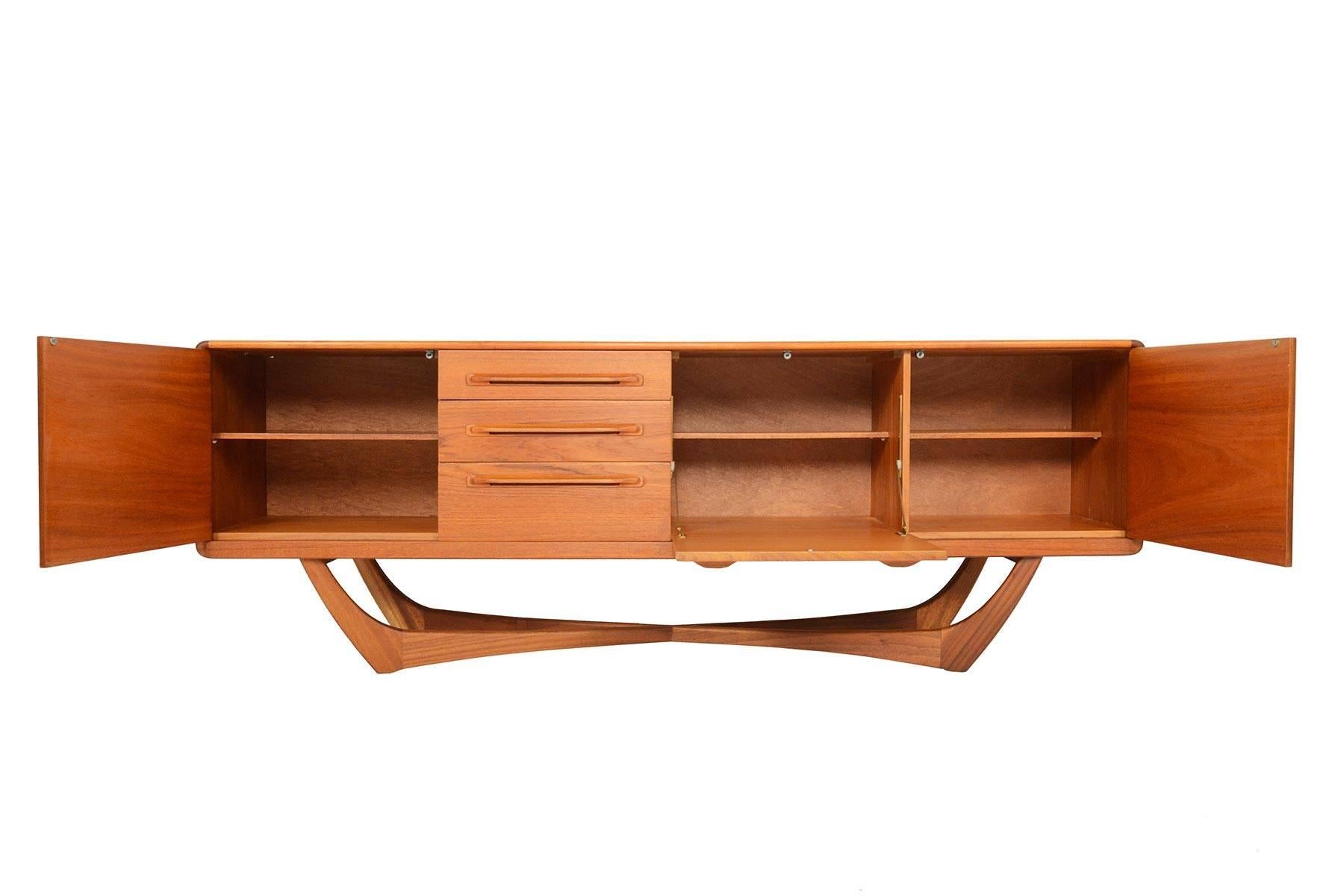 This exceptional Scottish modern teak credenza by Beithcraft is a rare find. The case sits on a dramatic parabolic X-form base. The left and right bays open to reveal a removable shelf. The center bar drops down to provide a serving platform. A bank