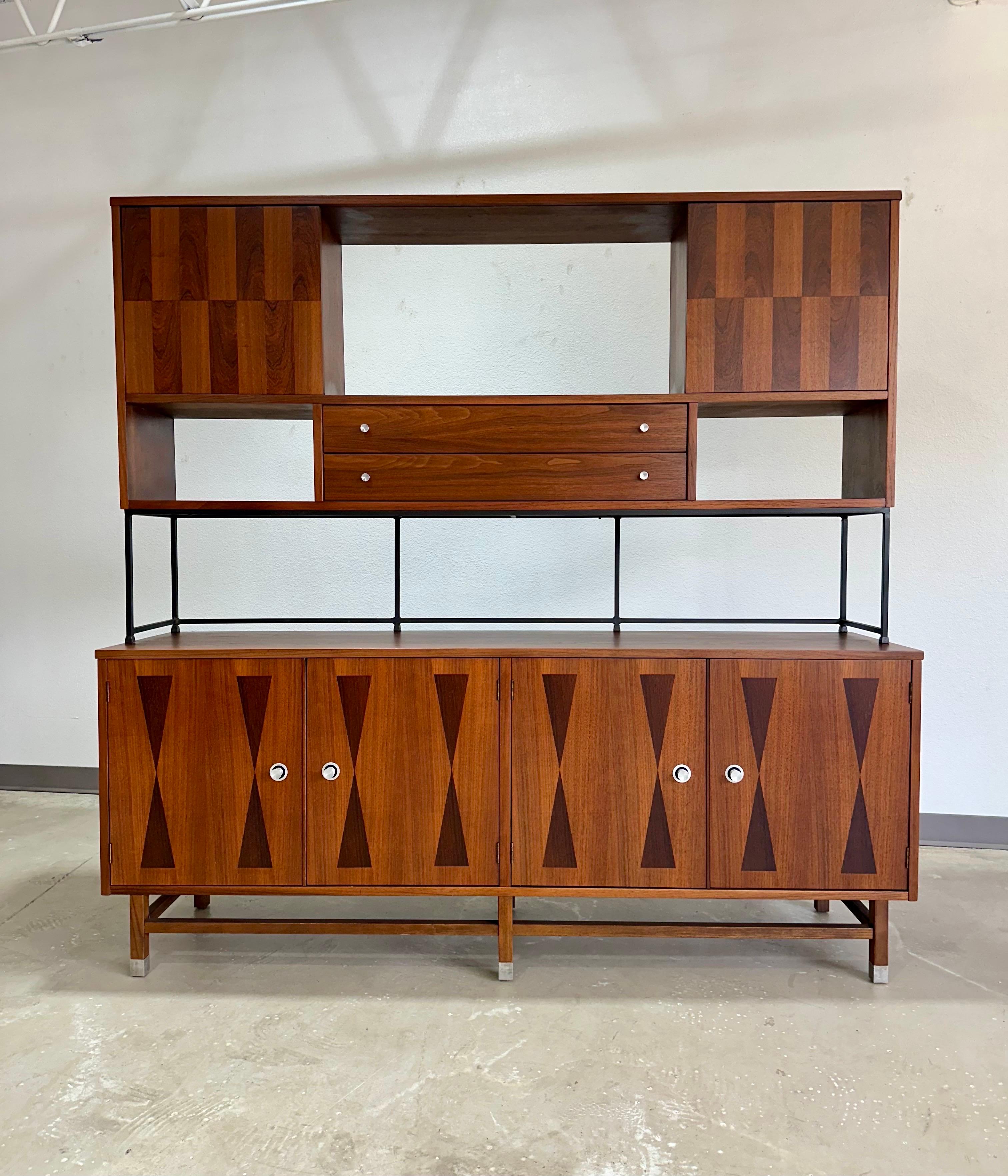 Fully Refinished Mid Century Modern Walnut and Rosewood Two Piece Wall Unit Display Cabinet by Stanley. Upper section rests freely on a black iron frame and features two sliding doors with walnut and rosewood checkered veneer, open cubbies and two