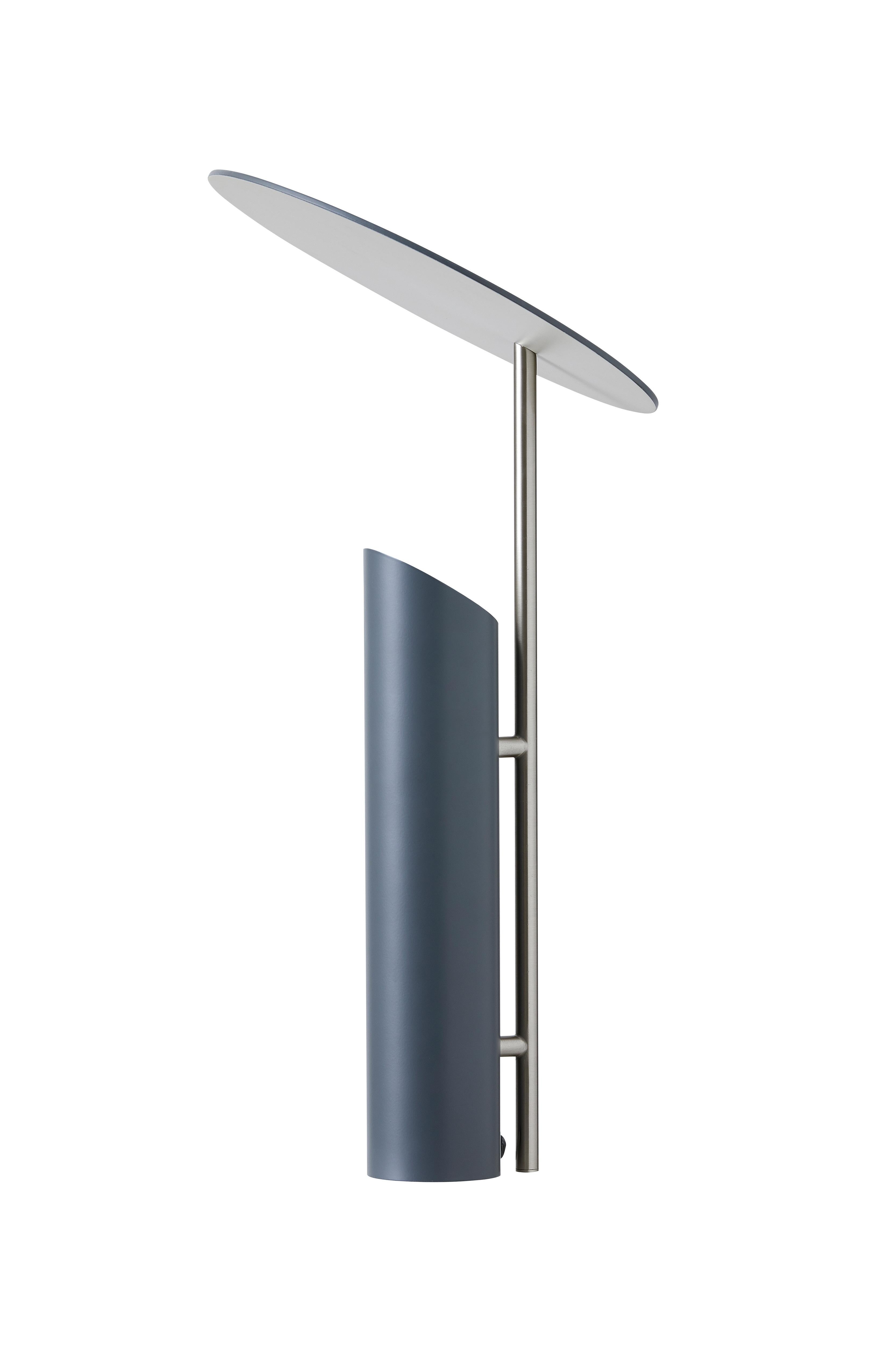 Table lamp with slanted disc shade which reflects the light coming from the base of the lamp (Light source facing upwards).

Material: 
All parts manufactured in steel
Powder coated grey
Gray variant; vertical rod in satin finish 
The down