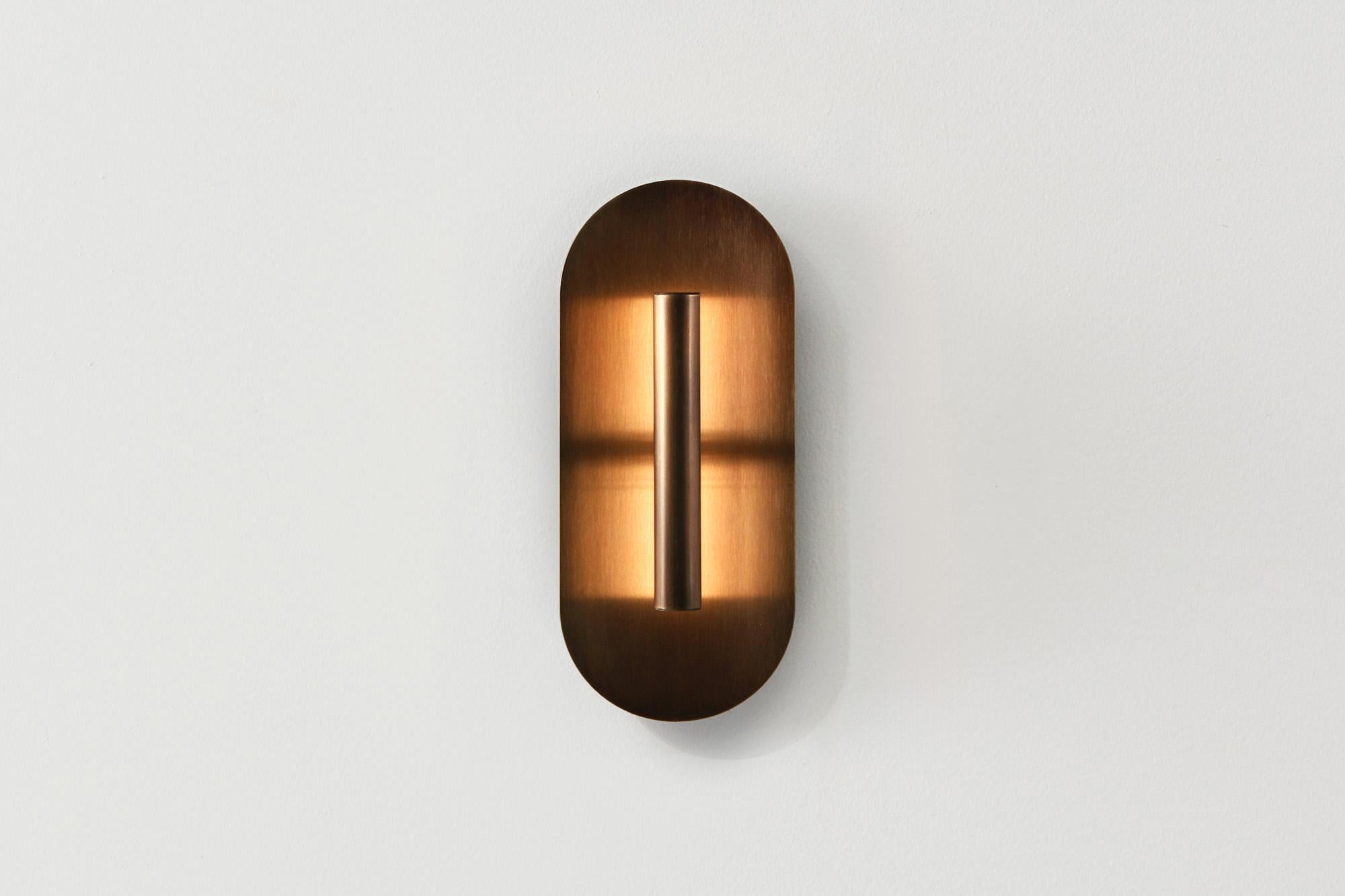Eine leistungsstarke LED-Lichtquelle wird von einer zart geschwungenen Schale reflektiert, die den Raum mit einem weichen, indirekten Licht erhellt.  
Die Patina-Bronze im Studio hat eine tiefe, schokoladige Oberfläche, die jedem Interieur ein