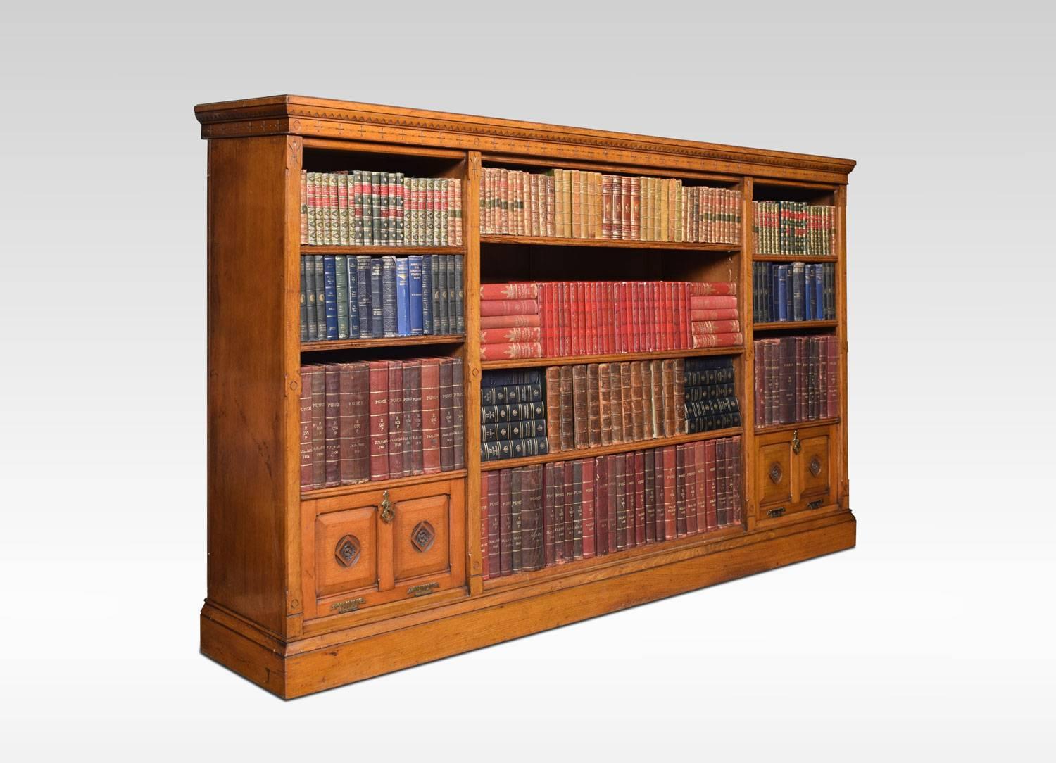 Reformed Gothic golden oak open bookcase, the large rectangular moulded top with carved ebonized freeze. Above three bays of adjustable shelves, the side sections fitted with small cupboards. All raised up on plinth base.
Dimensions:
Height 54