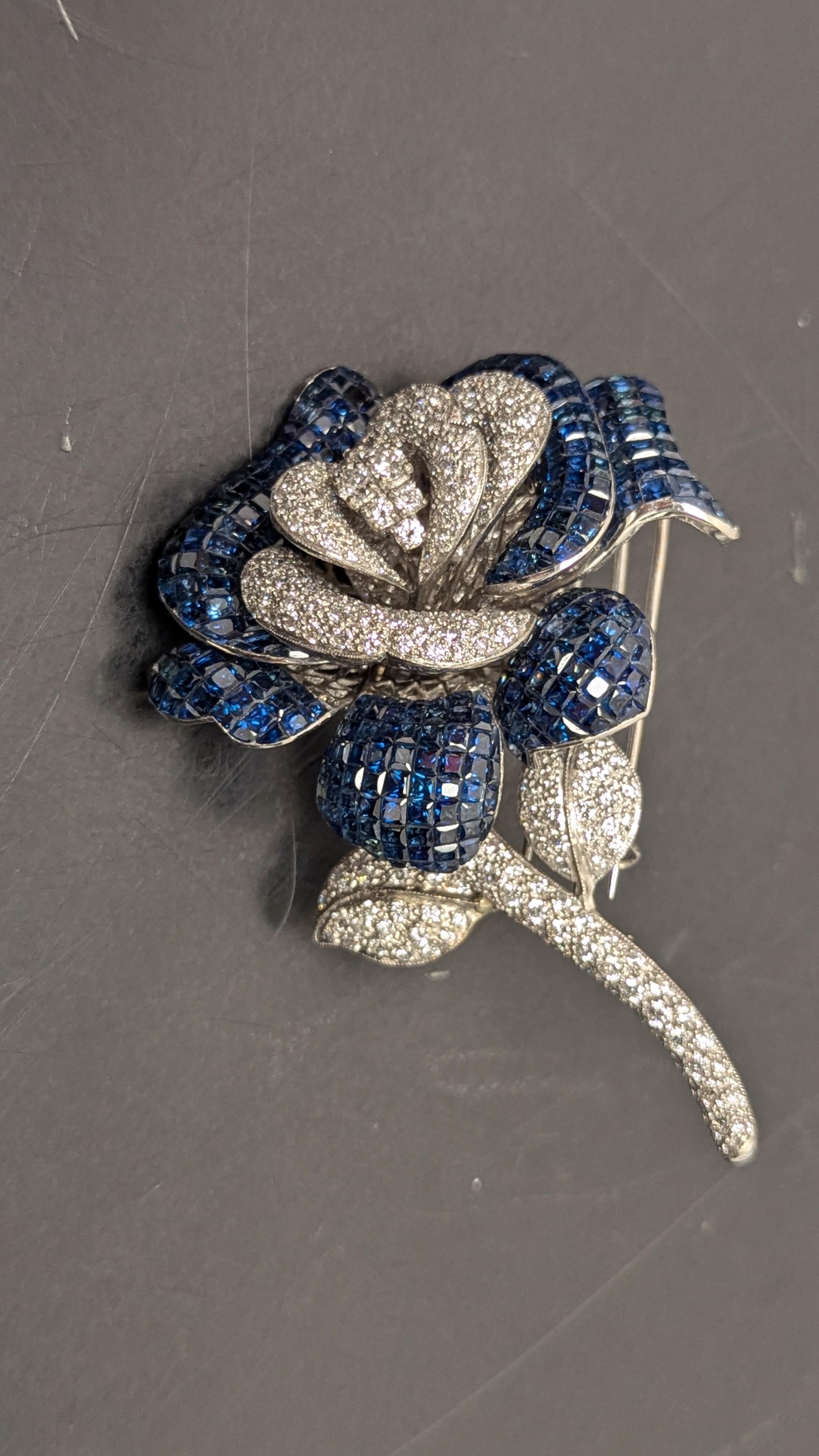 This intricately designed pavé-set diamond flower brooch with extending calibré-cut sapphire undulating petals comprises of approximately 40ct of square cut, invisible set sapphires and approximately 20ct of round, pave diamonds, mounted in 18K