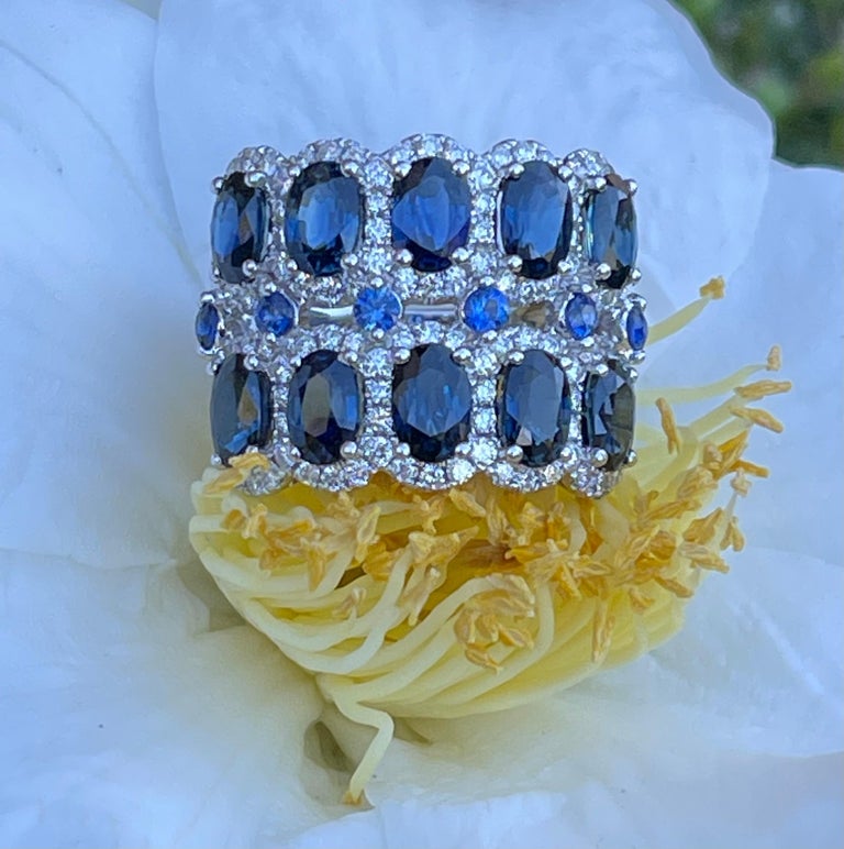 Exquisite and very regal looking, 18 karat white gold estate sapphire and diamond double wide band ring features two rows of beautiful natural blue faceted oval shaped sapphires, each surrounded and accentuated by a halo of round brilliant diamonds.