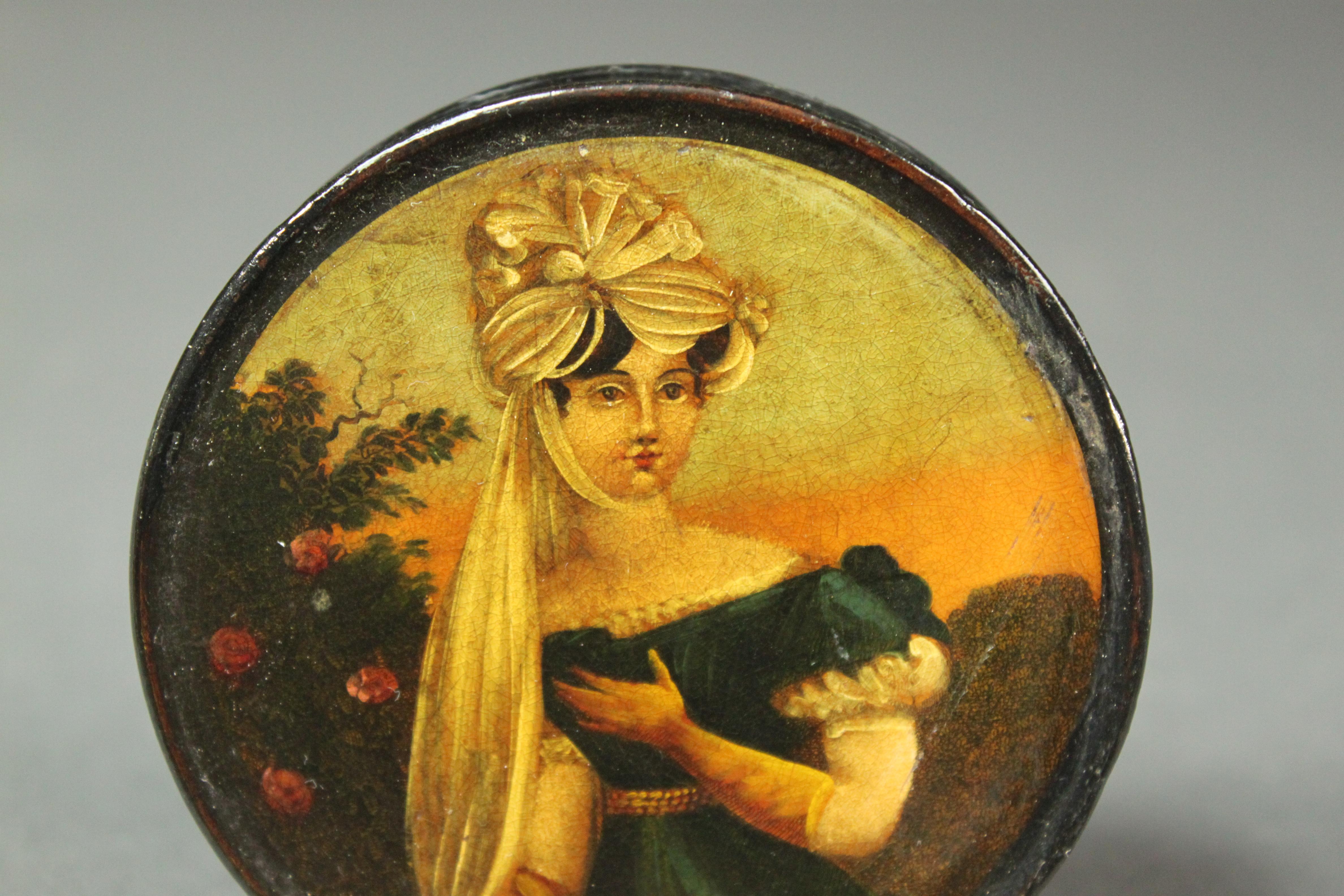 A Regency papier mâché snuff box with a painting of a lady wearing an elaborate headdress.