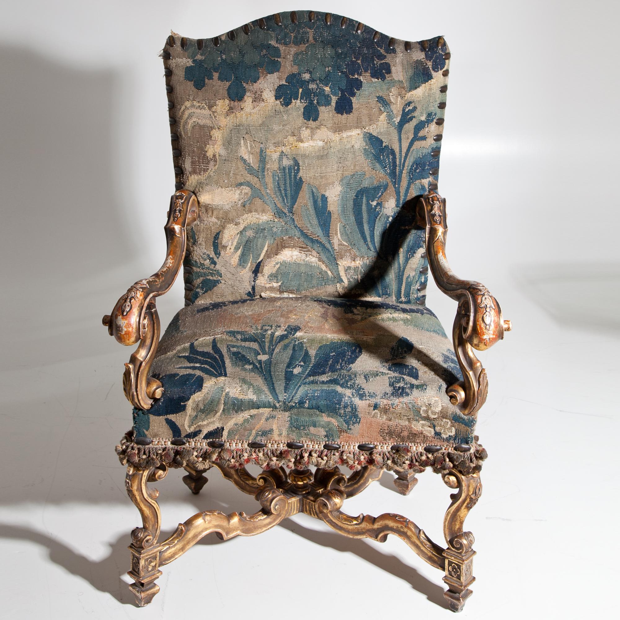 Gilt armchair upholstered with a blue-beige gobelin, standing on a carved base with X-strutting. The armrests end in volutes circa 18th-19th century.