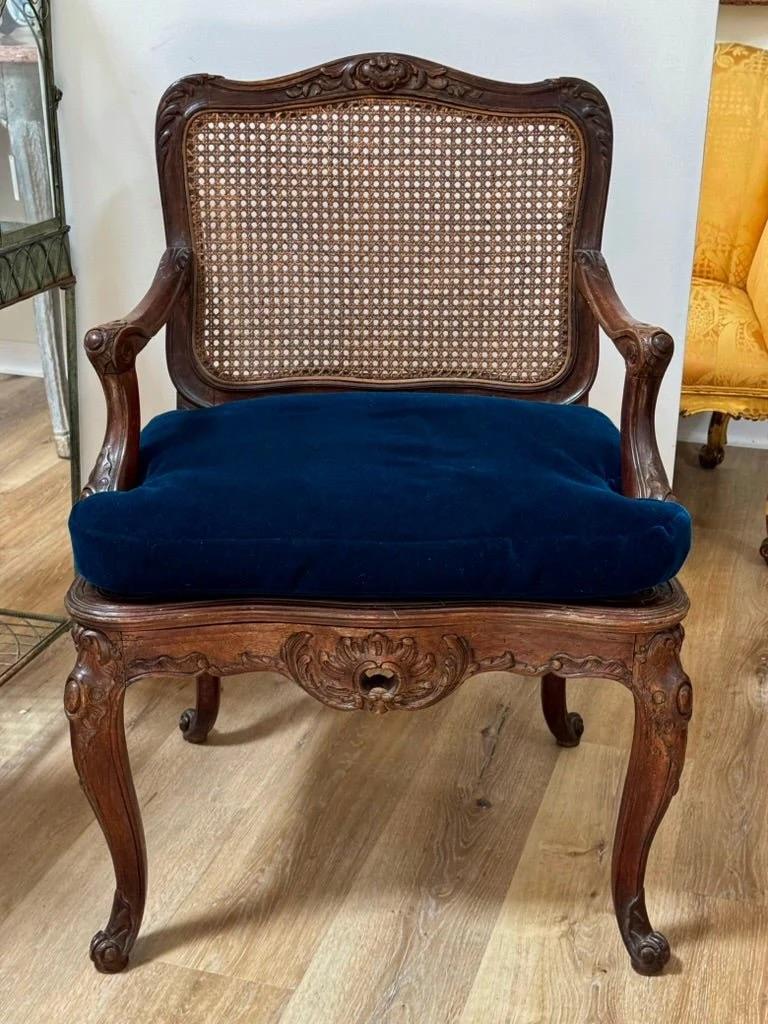 Regence Beechwood Caned Fauteuil, France, 18th century, the foliate carved top rail above the caned back rest, sided by volute scrolled arms raised on shaped supports, the caned, serpentine seat with custom cushion above a conforming seat rail with