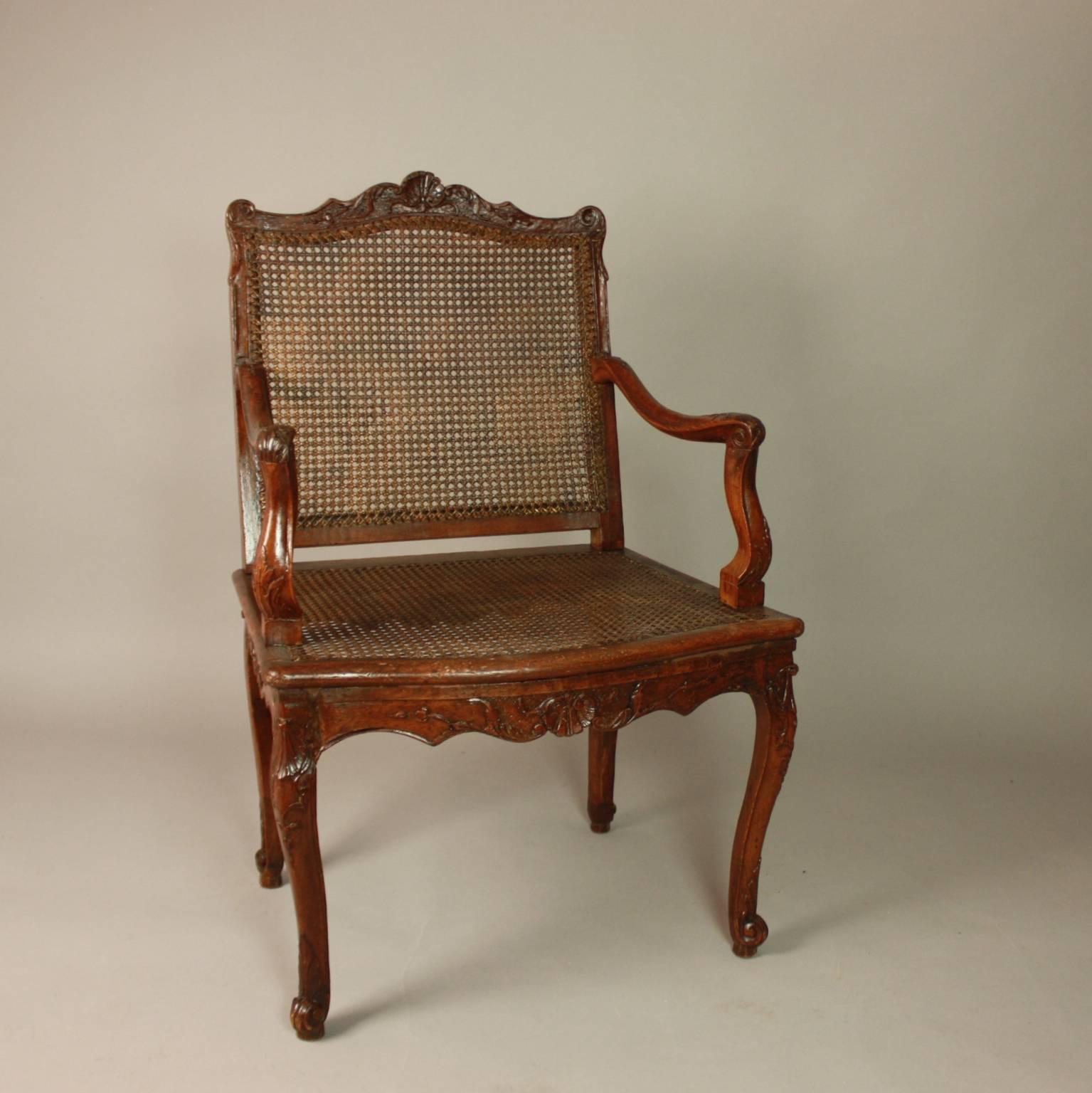 A beautiful Regence caned armchair with a finely carved decoration featuring a symmetrical design of shells, scrolls and pendants of flowers. The back and seat are caned with a rather close mesh. The rectangular back with fine carving on the top