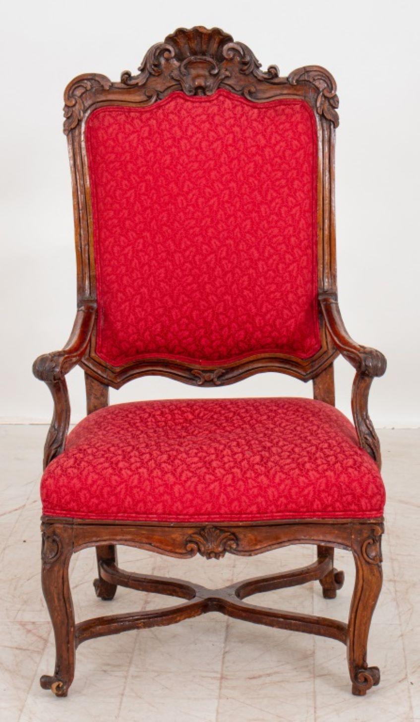Regence Carved Fauteuil a la Reine, with ornate crestrail with carved rocailles, largely 18th century with 19th century restorations, above a damask upholstered back with down swept arms terminating in scrolling volutes, above a damask seat on shell