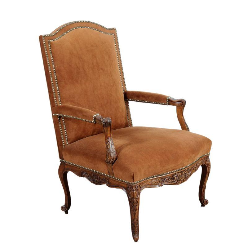 A carved wood Regence style fauteuil with cabriole legs, arched back, carved details to apron, legs and arms with a light brown soft suede like fabric and nail head trim. A stately, elegant chair would make a beautiful addition to a library, living