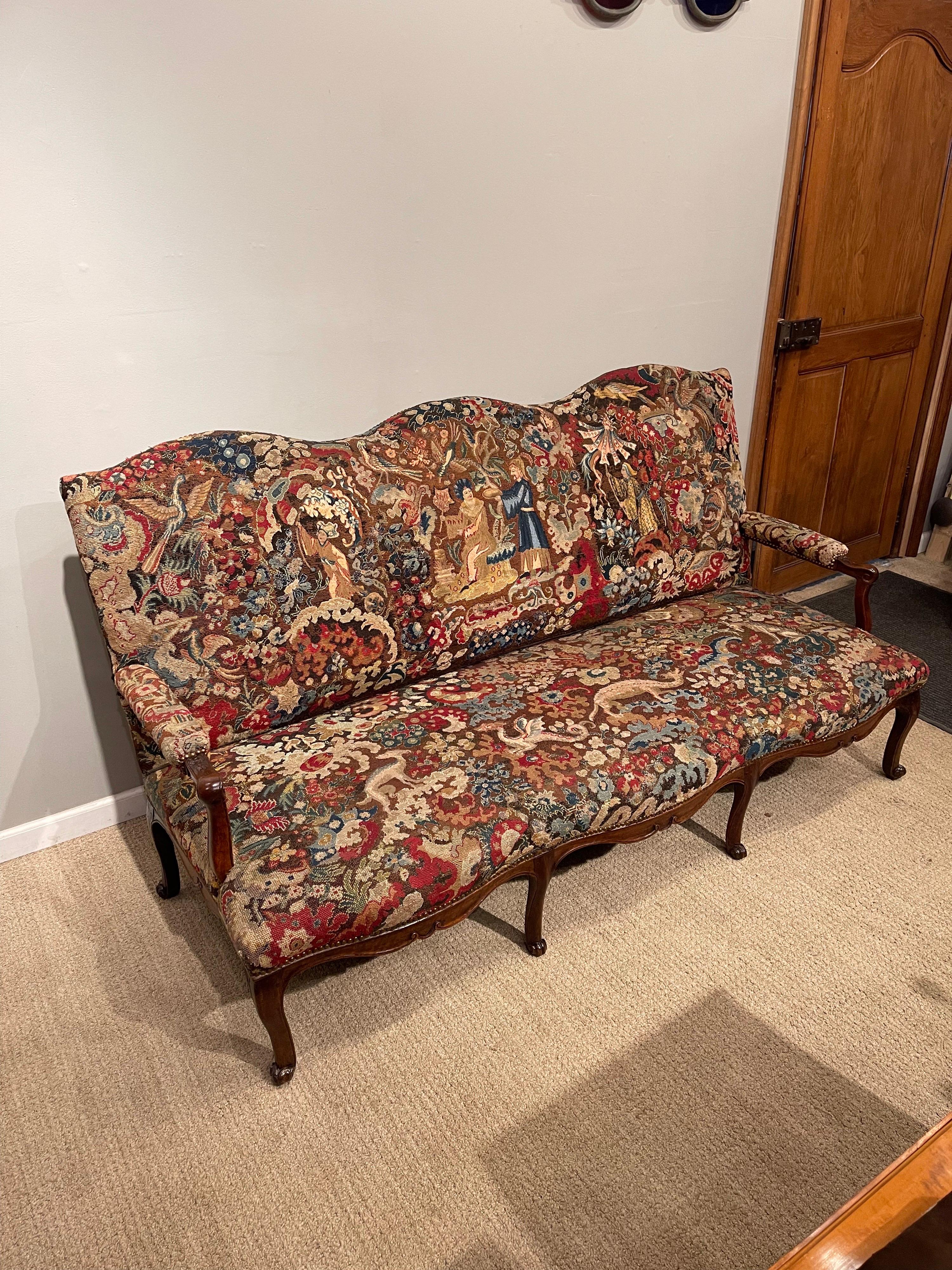 A fine Regence period needlepoint covered settee
with shaped upholstered back and carved & padded scrolling arms over
conforming upholstered seat; the back, arms & seats covered in multi-colored 
Needlepoint with chinoiserie figures, dragons and