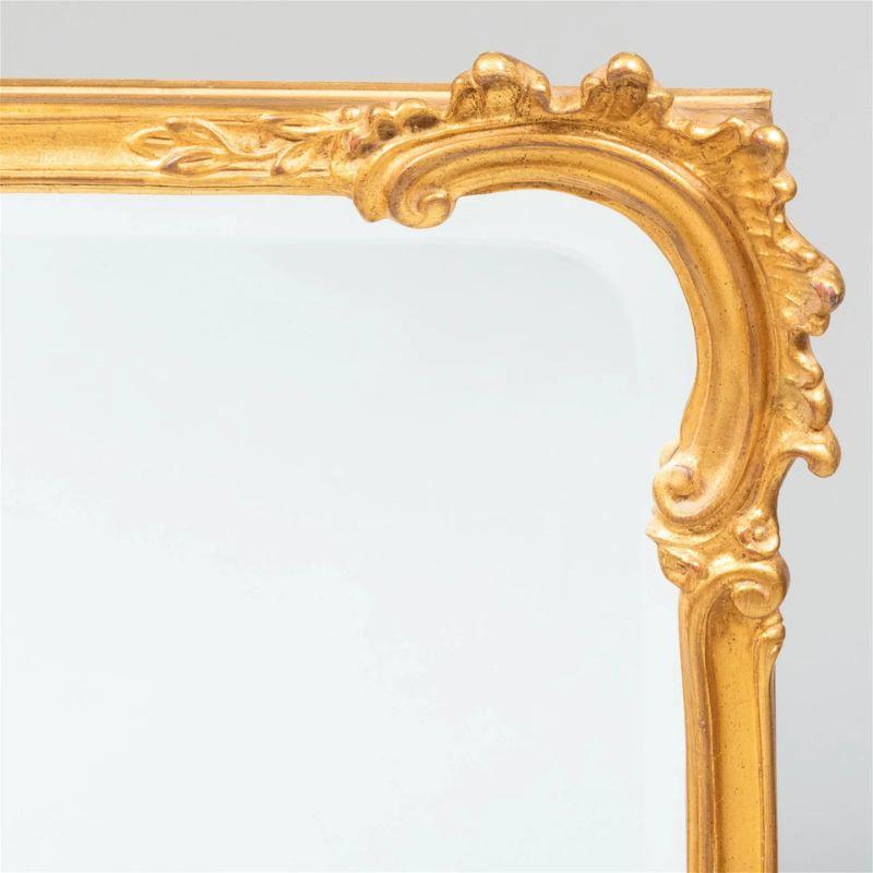 A gilt Regence style wall mirror with symmetrical curved scroll details to corners and center of each mirror frame.
