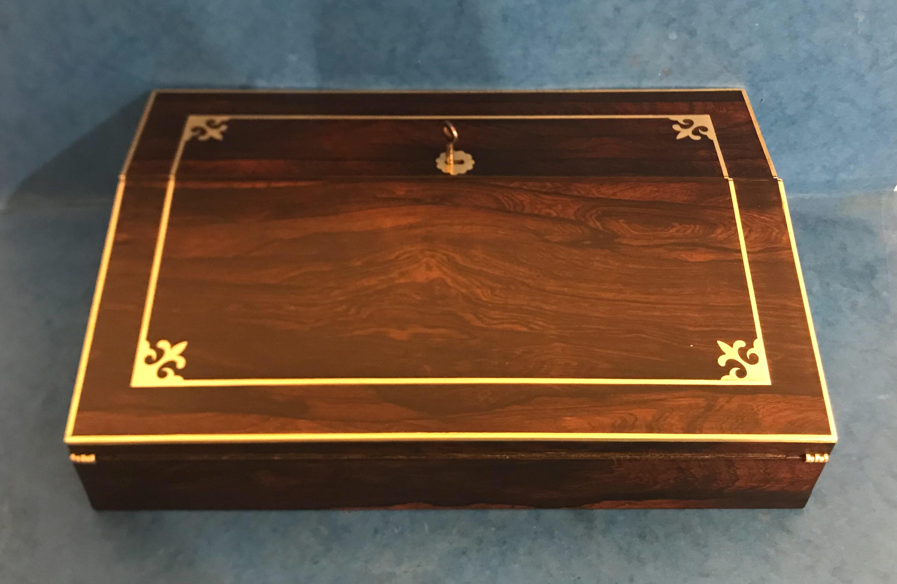 A Regency 1820 Brass inlaid rosewood lap desk, with inset brass handles, are leathered writing surface and two original ink wells, it has a stationary rack to the interior and various lidded compartments for nibs and pens, unfortunately the lock