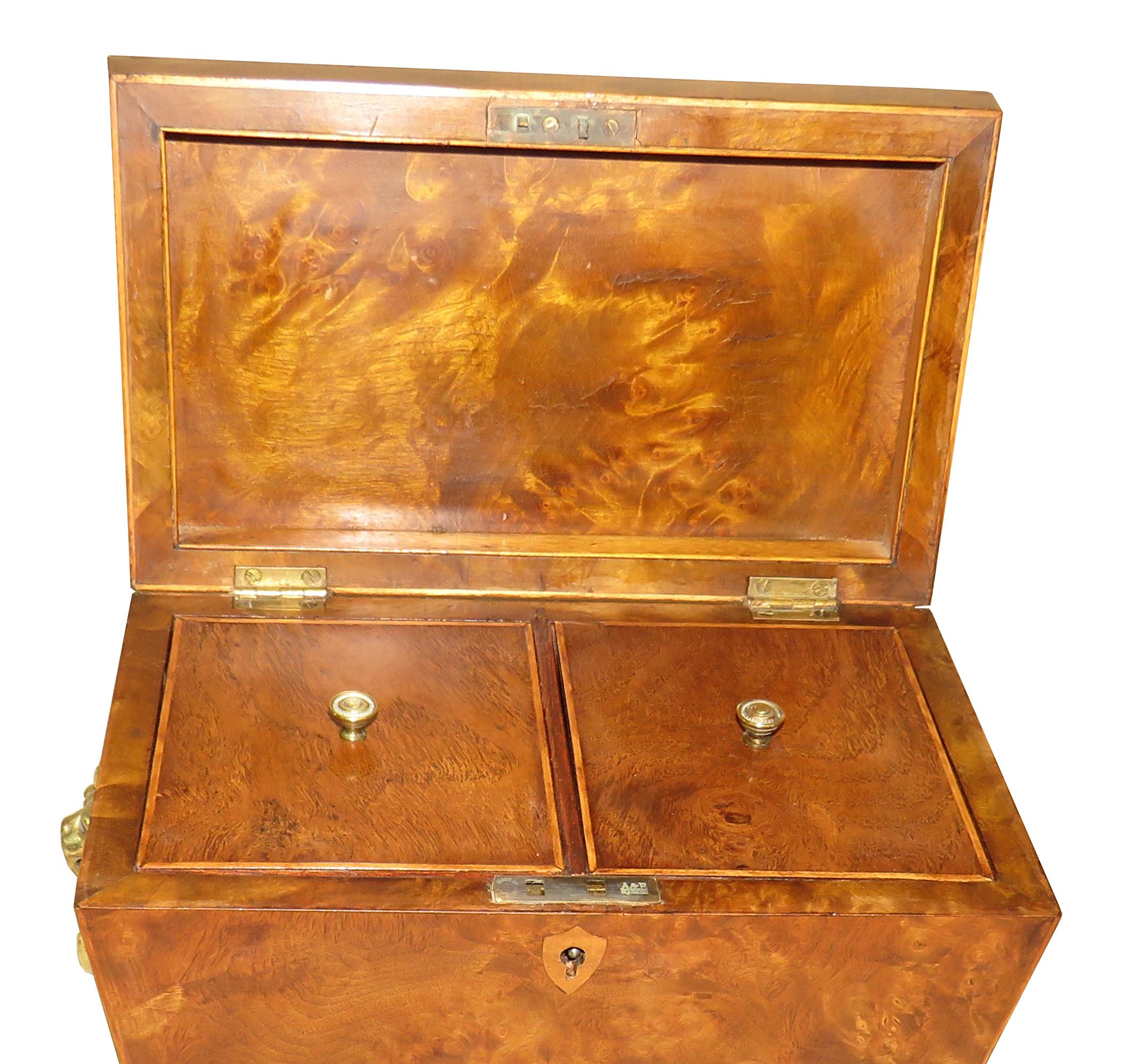 A Fine Quality Regency Period Burr Elm
Sarcophagus Shaped Tea Caddy having
Strung Decoration And Hinged Lid Enclosing
Lidded Divisions With Original Brass Lions
Mask Handles To Side Raised On Elegant
Original Brass Paw Feet

(This is a fine quality
