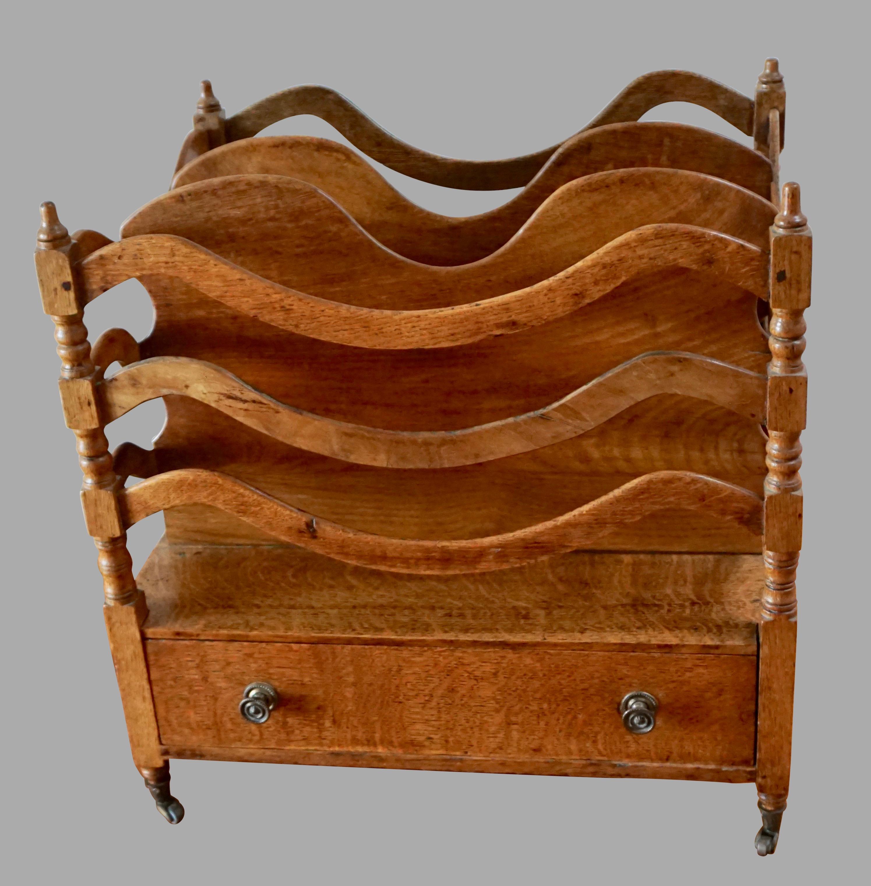 An English Regency period Canterbury of unusual undulating serpentine form, the sides and dividers above a single drawer with replaced metal knobs, all resting on short turned legs terminating in original brass casters, Circa 1800-1825.