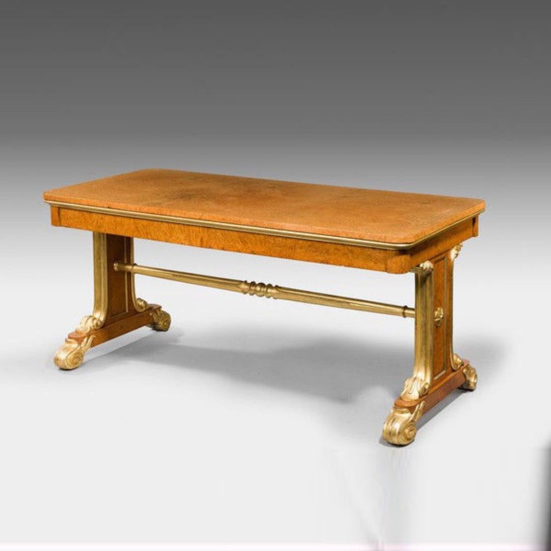 A Regency Amboyna and gilt library table attributed to Seddon and Morel, the rectangular top set upon solid end supports with a turned, reeded and gilded stretcher and gilded foliate bun feet, decorated throughout with rich amboyna veneers and gilt