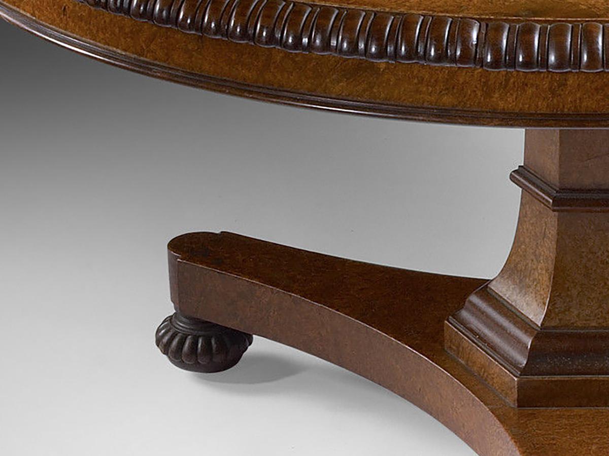 The burr figured and quarter-veneered top with egg and dart moulded edge and burr veneered frieze with moulded lip; above a spreading hexagonal pillar with central gaitered banding and ogee moulded collar below; on a triform platform base with