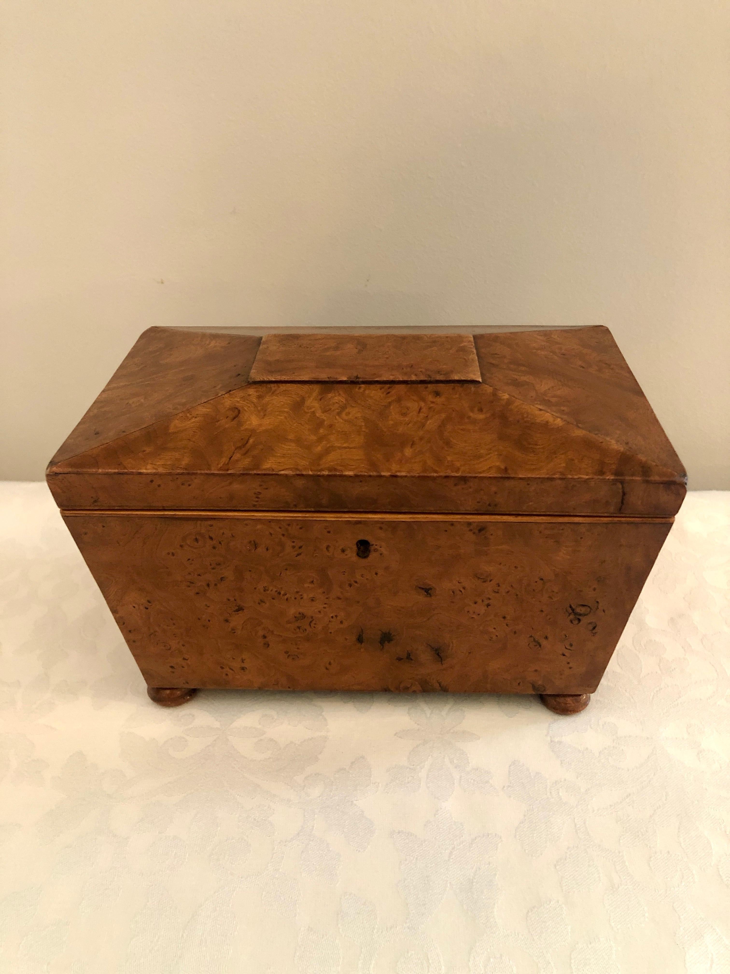 Regency antique 19th century burr elm tea caddy having a sarcophagus shaped lip which lifts to reveal two lidded compartments with original turned knobs, standing on small bun feet.

The color and patination are striking.

Measures: H 12.5cm
W