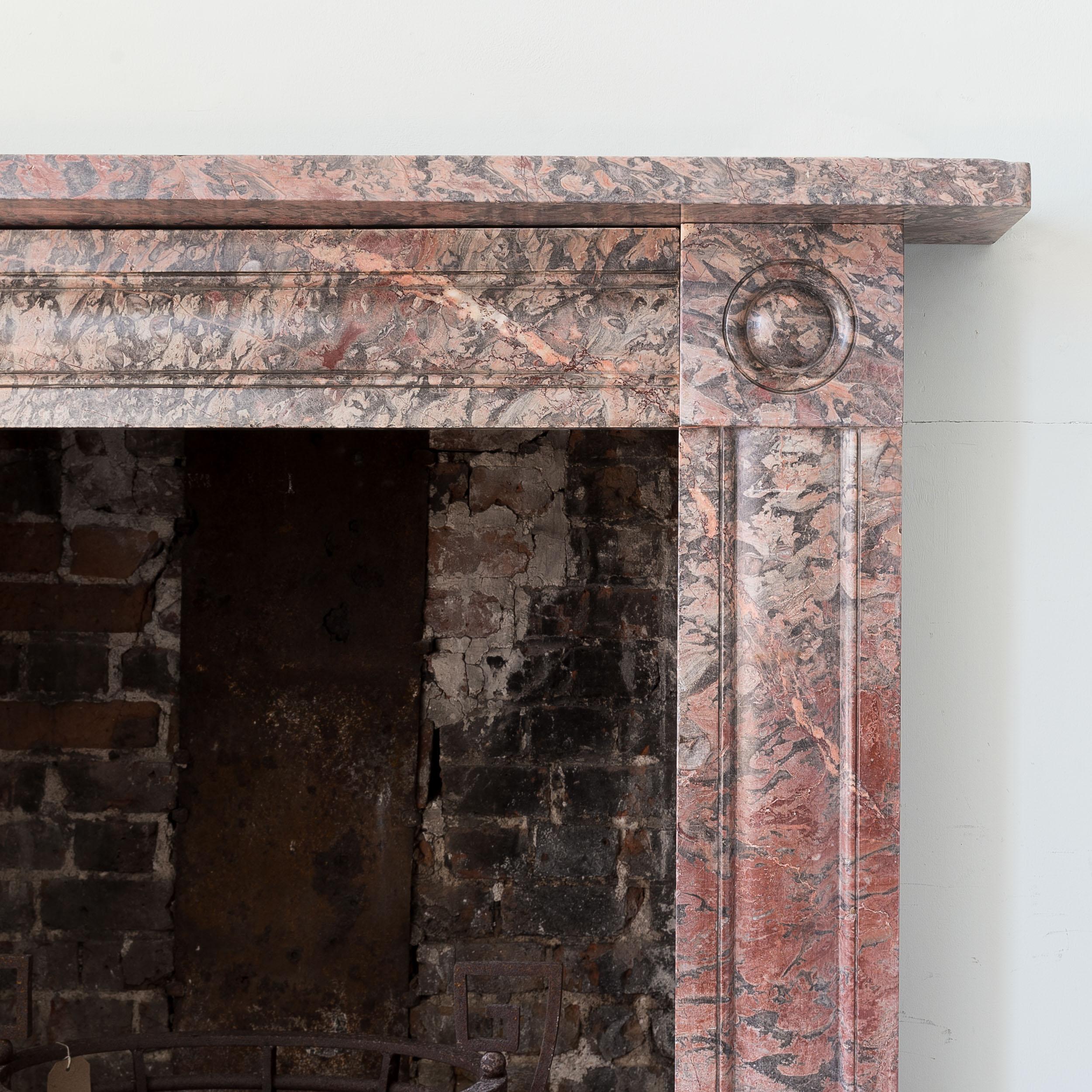 An English Regency period Devonian limestone fireplace, c.1820, with cushion moulded frieze and jambs, the corner-blocks with bull's-eye roundels, on square footblocks, realised in well figured material with good varied colouration.

Opening width
