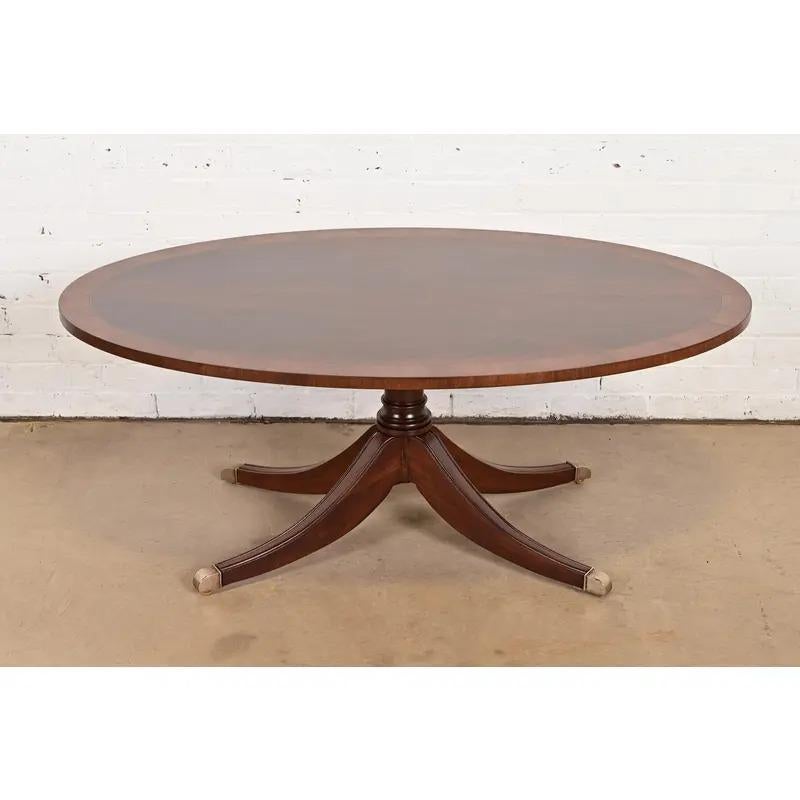 Magnifique table basse à piédestal de style géorgien ou régence

États-Unis, fin du 20e siècle

Magnifique plateau en acajou flammé, avec bandes en bois satiné, piédestal en acajou massif sculpté, et pieds coiffés de laiton.

Dimensions : 48,25 