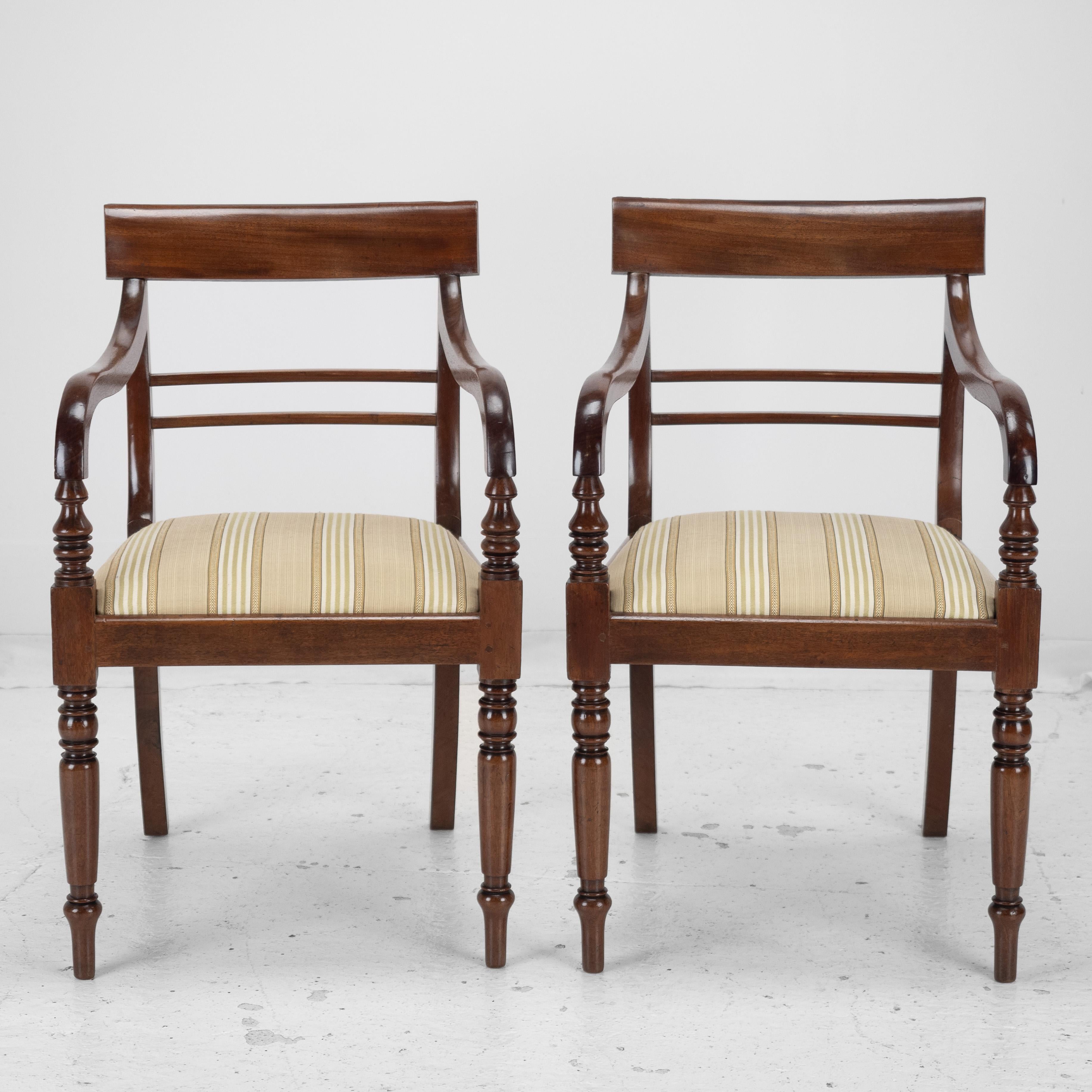 A pair of Regency period, mahogany elbow chairs or carvers, circa 1820. This pair features attractively figured timbers with curved top rails, over a double plain slat. Drop-in upholstered seats, covered in a quality woven Regency stripe fabric in