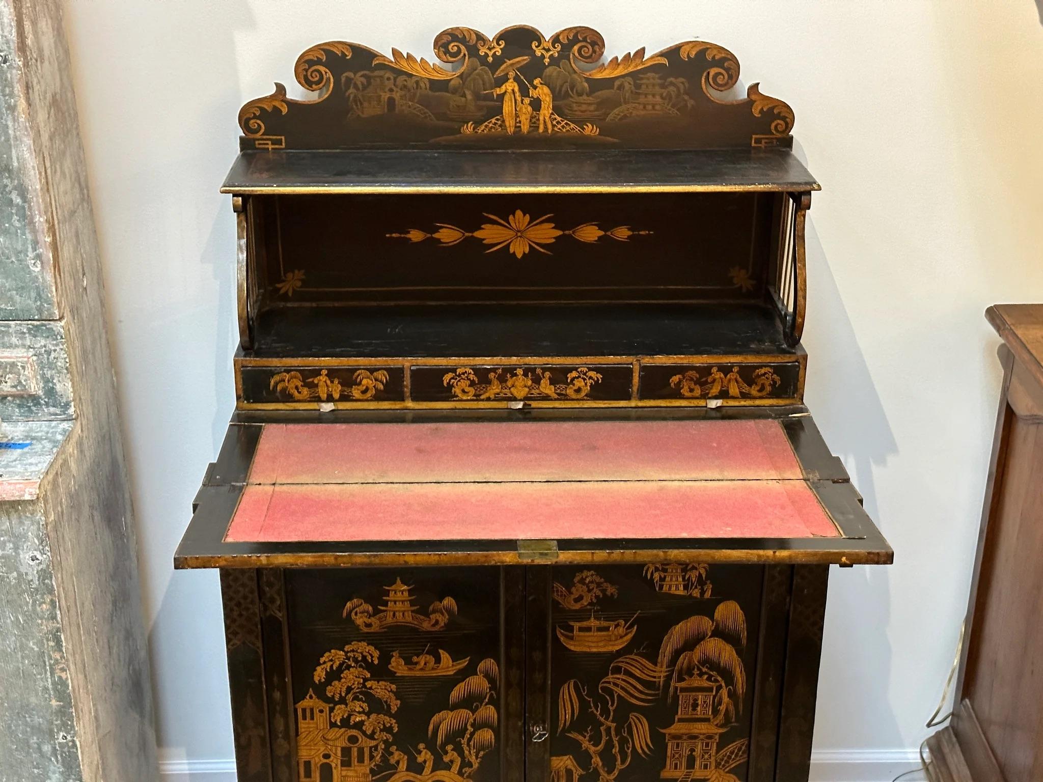 Regency Black Painted and Parcel-Gilt Chinoiserie Decorated Side Cabinet, from an installment by Colefax and Fowler.  In two parts, the top section having a shelf and three concealed drawers, the lower portion with a drop down writing surface over a
