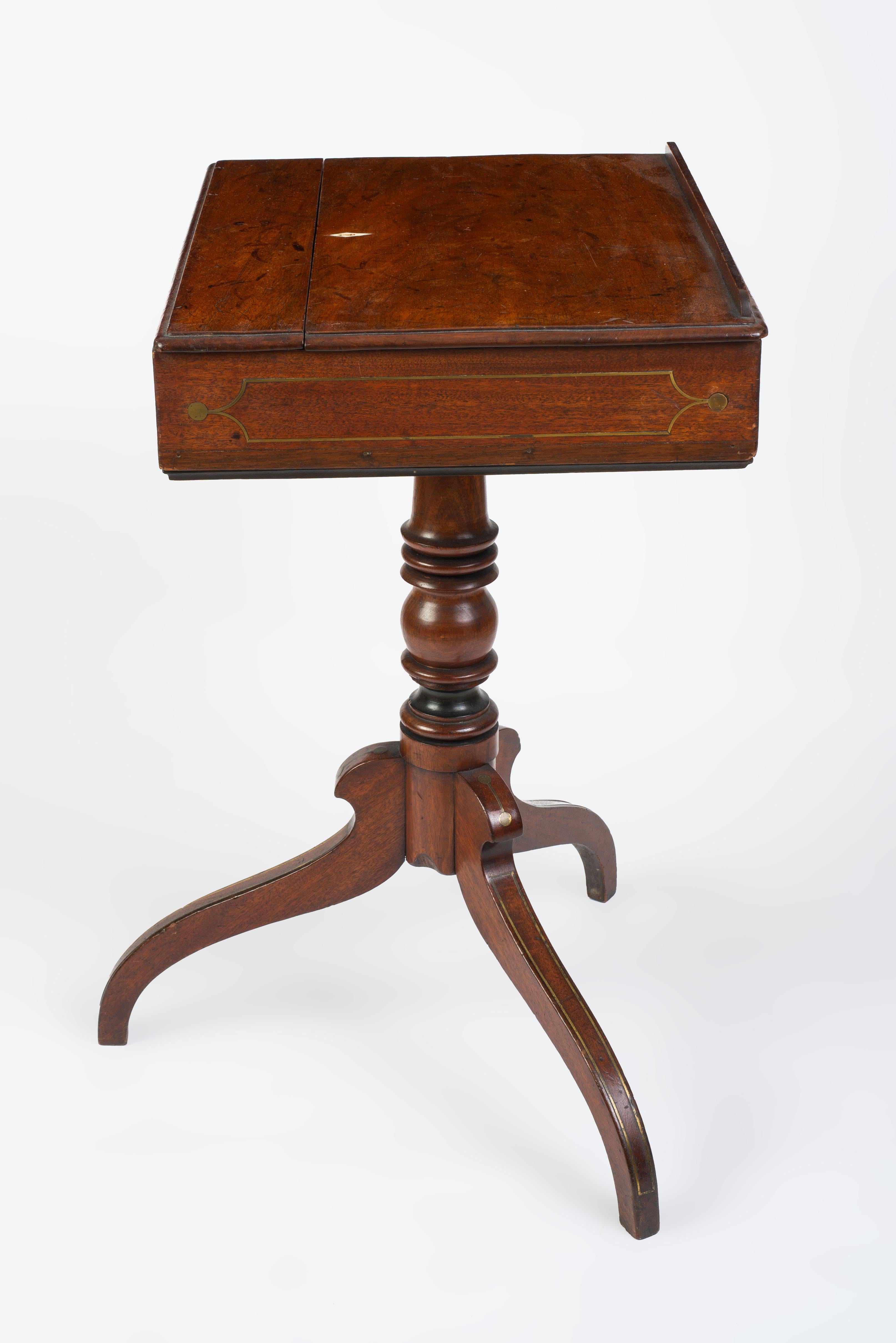 The hinged ratcheted top above a brass inlaid frieze raised on a turned pedestal ending in a brass-inlaid tripod base. The inside lined with the original worn marbled end paper.