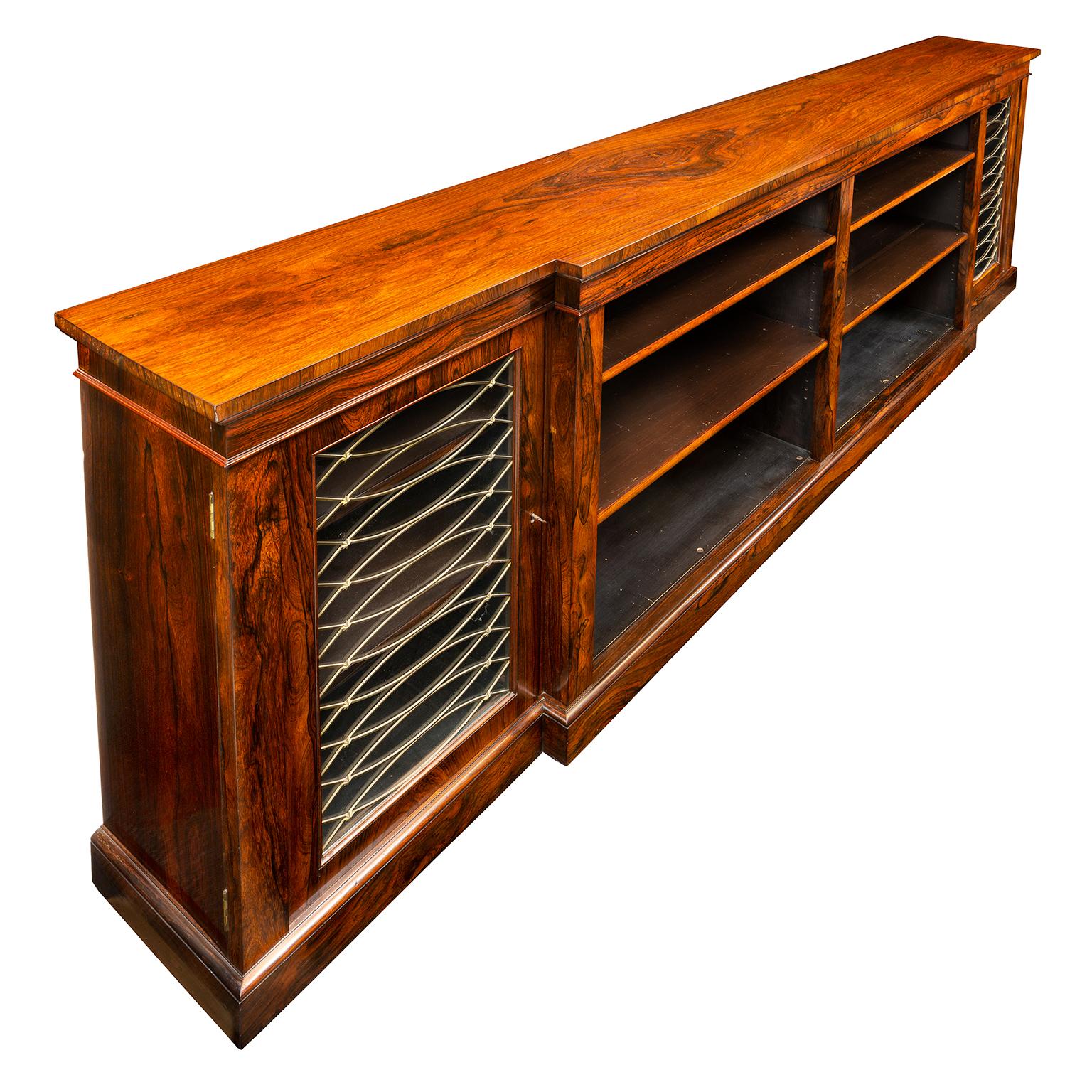 A fine Regency rosewood side cabinet/bookcase. The break-front top above two open compartments of adjustable book shelves flanked by glazed side cabinets with gilt grilles composed of curved lattice bars studded with star shaped adornments. The back