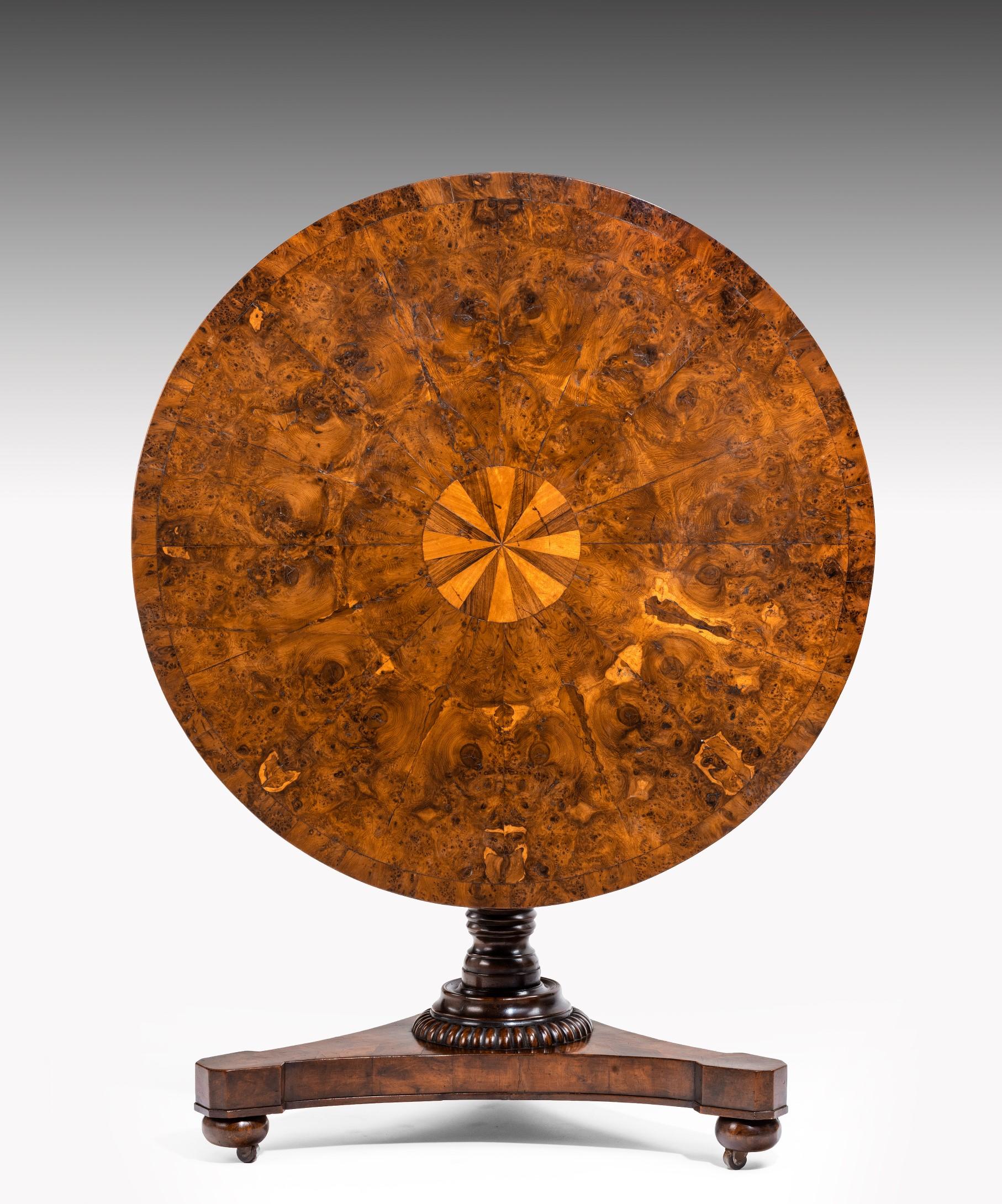 A Regency period centre table veneered in burr yew; the table's top segment veneered in yew wood with a central inlayed circle of satinwood and rosewood; the table is raised on a turned stem which terminates in a triform base.

This centre table
