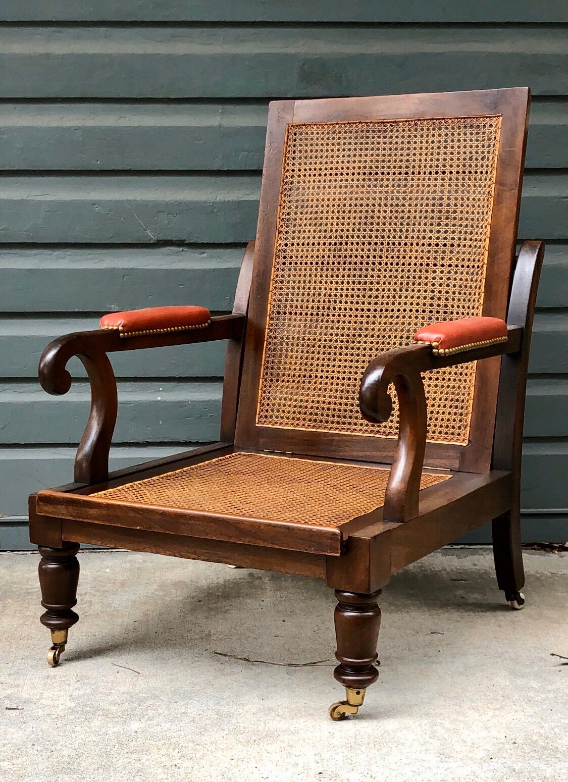 Regency period mahogany Campaign library bergère chair having a removable sliding cane seat and back. This chair has scrolled arms above turned tapered legs with brass casters.