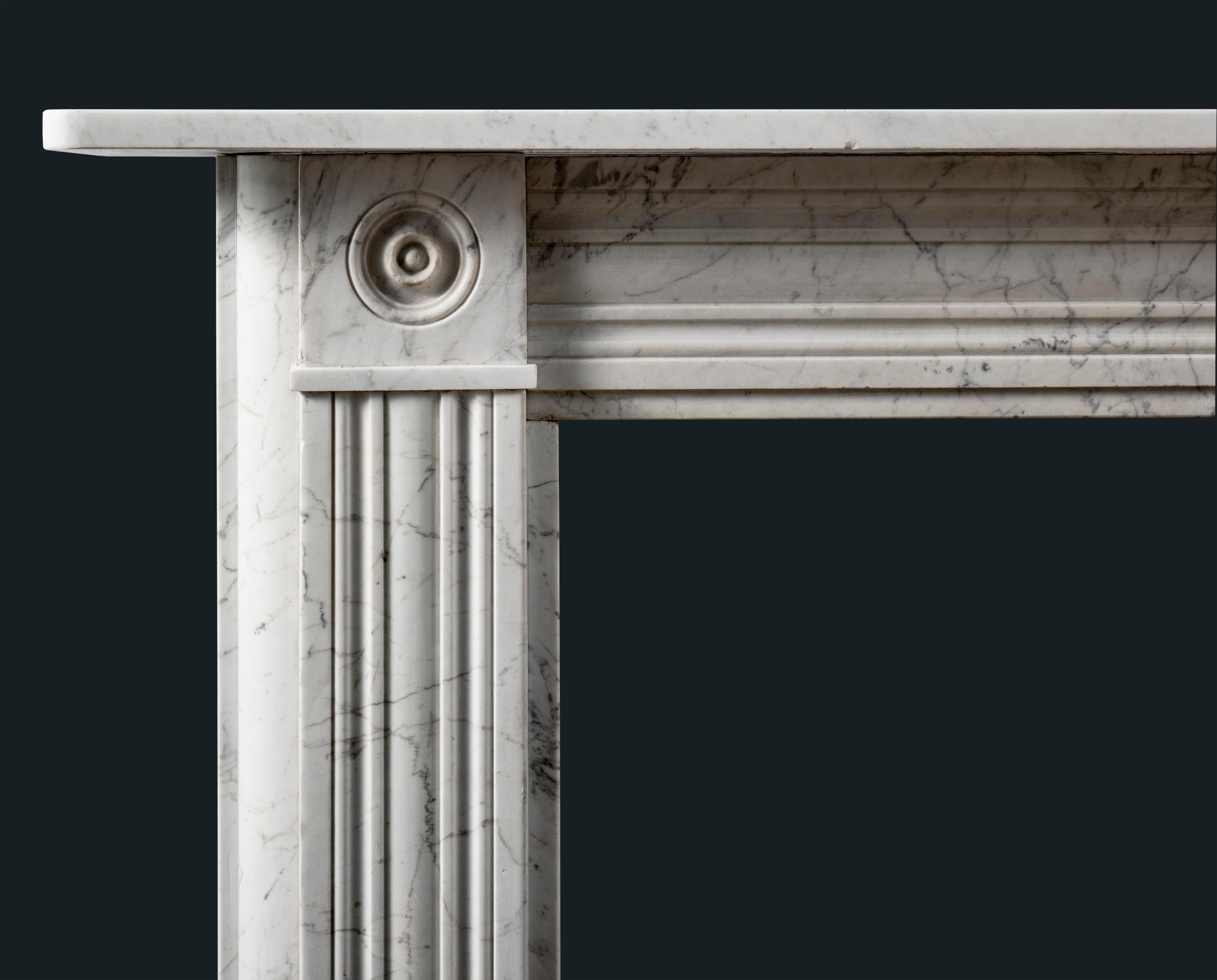 An antique Georgian/Regency veined Carrara Marble Bullseye fireplace surround, with concave and convex channel moulds to the frieze and jambs, the corner-blocks composed of convex roundels typical of the period.

English, c.1810.

This elegant