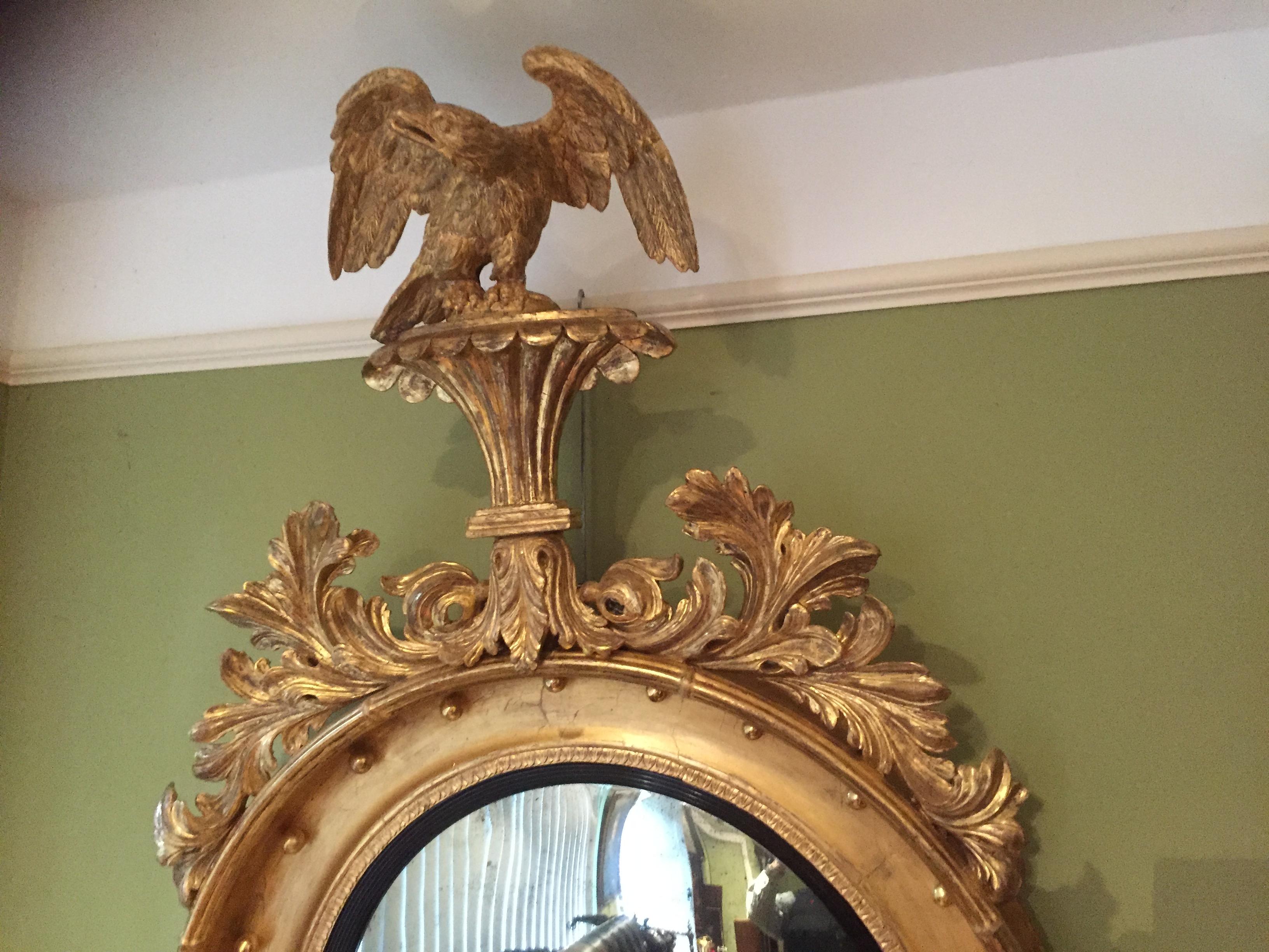 The carved eagle stands on a fluted platform above a carved leaf decorated applied mount. The circular giltwood and gesso frame with an old mercury plate and ebonized reeded mount sits above a crisply carved decoration.