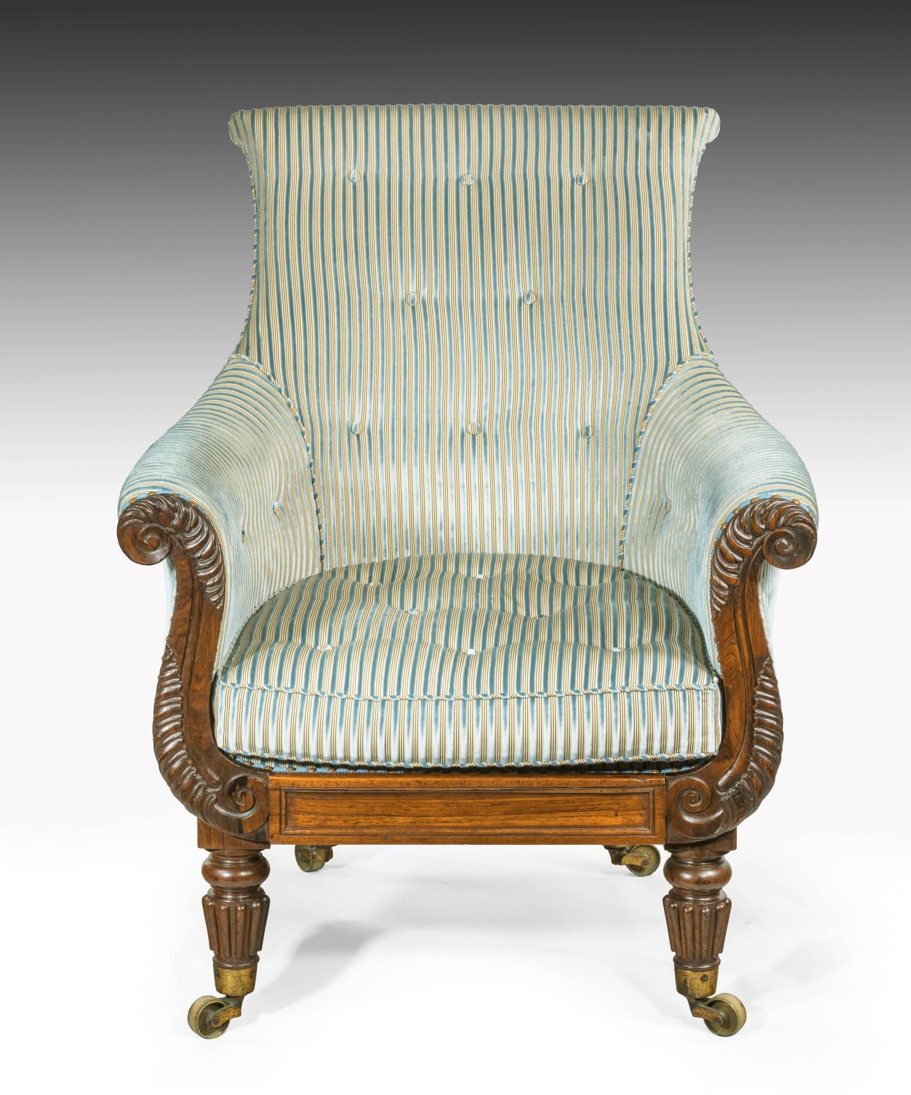 A generous Regency period carved rosewood library armchair; the armchair's upholstered back and seat above scrolling showwood armchs crisply carved with acanthus leaves and a panelled seat rail; raised on turned and reeded legs which terminate in
