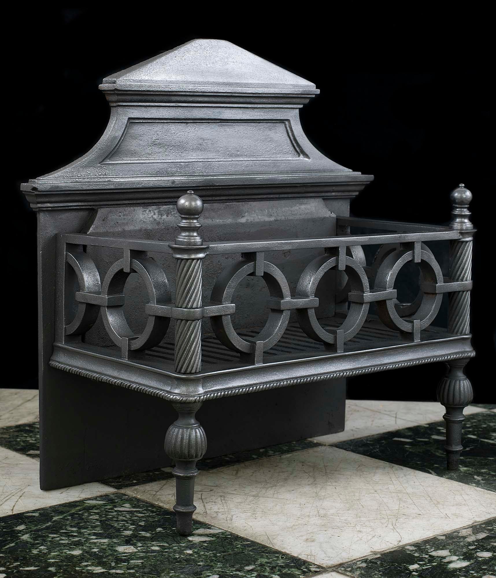 A heavy Regency cast iron fire grate with a pediment backplate, linked circles forming the grate front and sides, sturdy barley twist standards topped by small round finials and terminating in reeded bulbous, pegged feet, English, circa 1830.
   