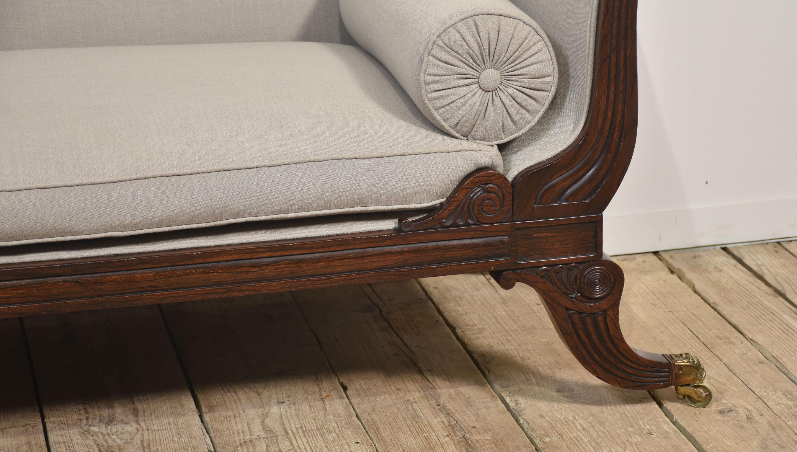 Chaise Lounge Regency - Con una barra trasera tallada sobre un respaldo tapizado, un elegante brazo en volutas y un asiento con cojín suelto. La pieza se apoya en patas de sable elegantemente curvadas, acabadas con casquillos y ruedas de