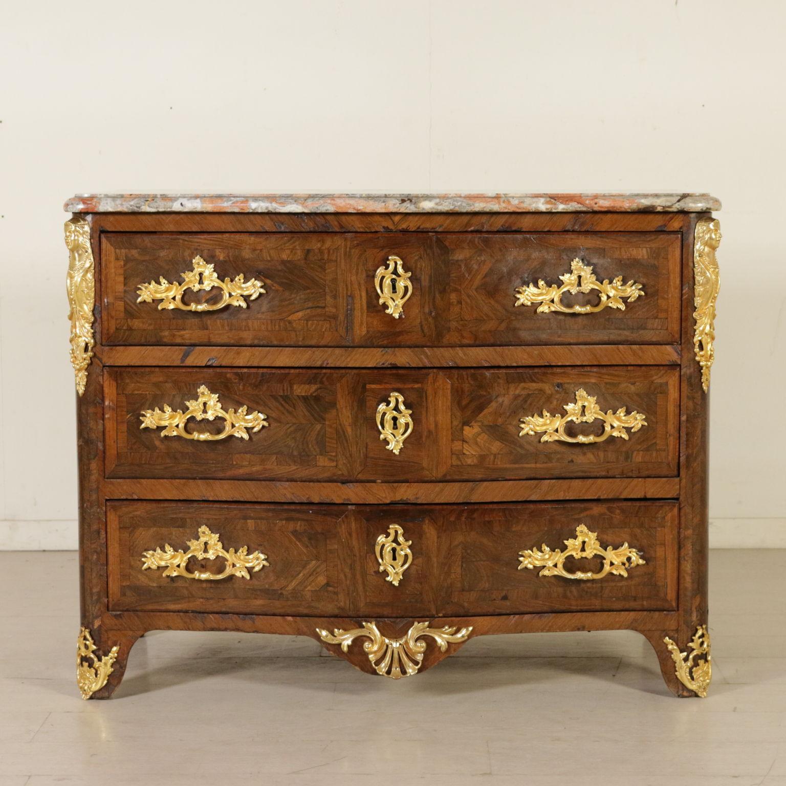 An elegant Regency chest of drawers, serpentine front. Three drawers and wide skirt. Bipartite and quadripartite wood reserves and borders. Embellished with friezes and gilded bronze handle, partly replaced. Shaped marble top. Manufactured in