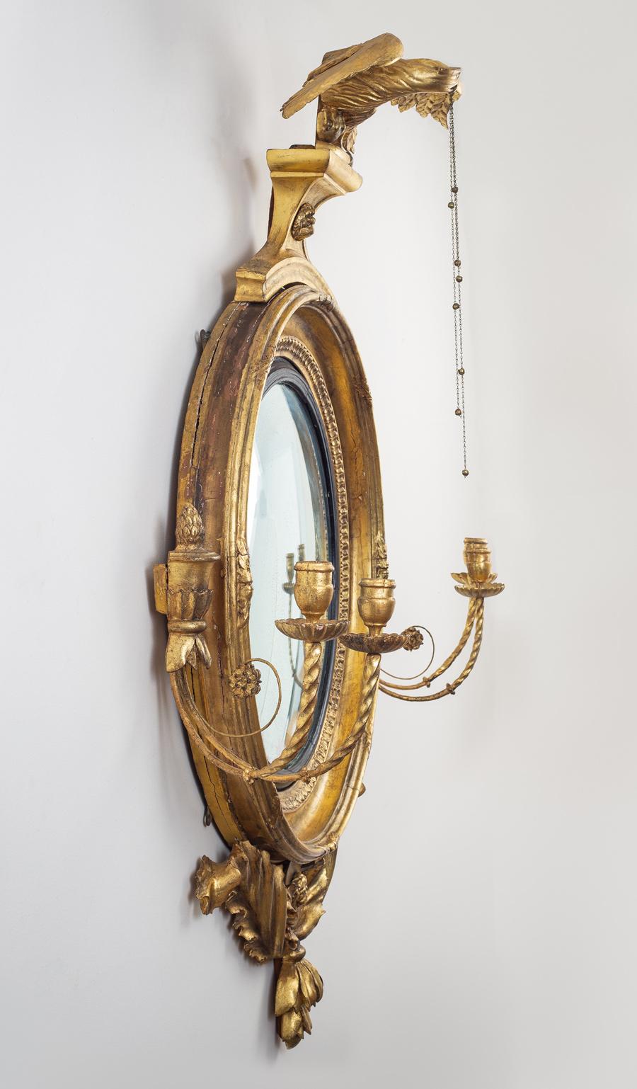 Large monumental classical gilded convex girandole mirror with strikingly well-carved dynamic eagle holding three chains, double candle arms that emanate from a shaped vase flank the mirror frame, the undermount has deeply carved acanthus leaves and