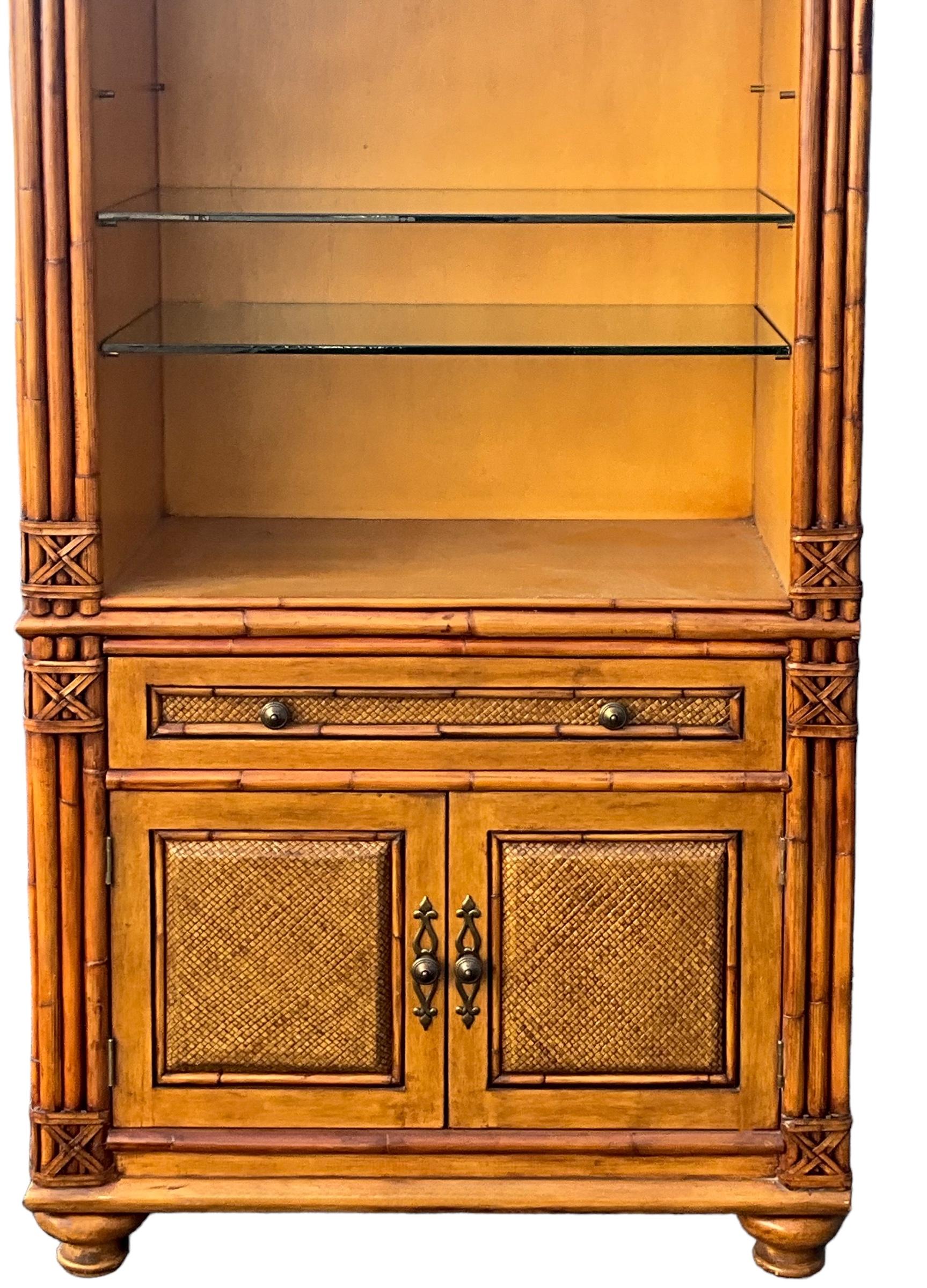 This is a set of regency style carved fruitwood faux bamboo style cabinets. They are able to be lit, and the glass shelves are adjustable. Each cabinet has a single drawer over two doors. The sides are a stained faux grasscloth. They are