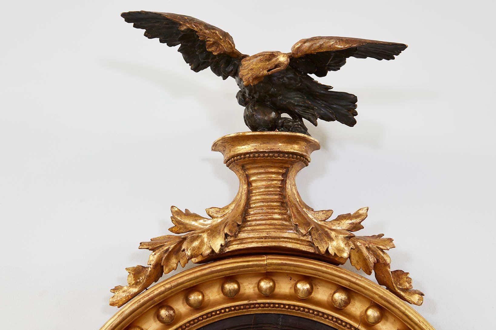 Fine Regency giltwood convex mirror, the ebonized eagle with gilt head and shoulders standing on ribbed plinth with acanthus leaf supports, the turned frame with gilt balls and beaded molding and ebonized slip surrounding original convex mercury