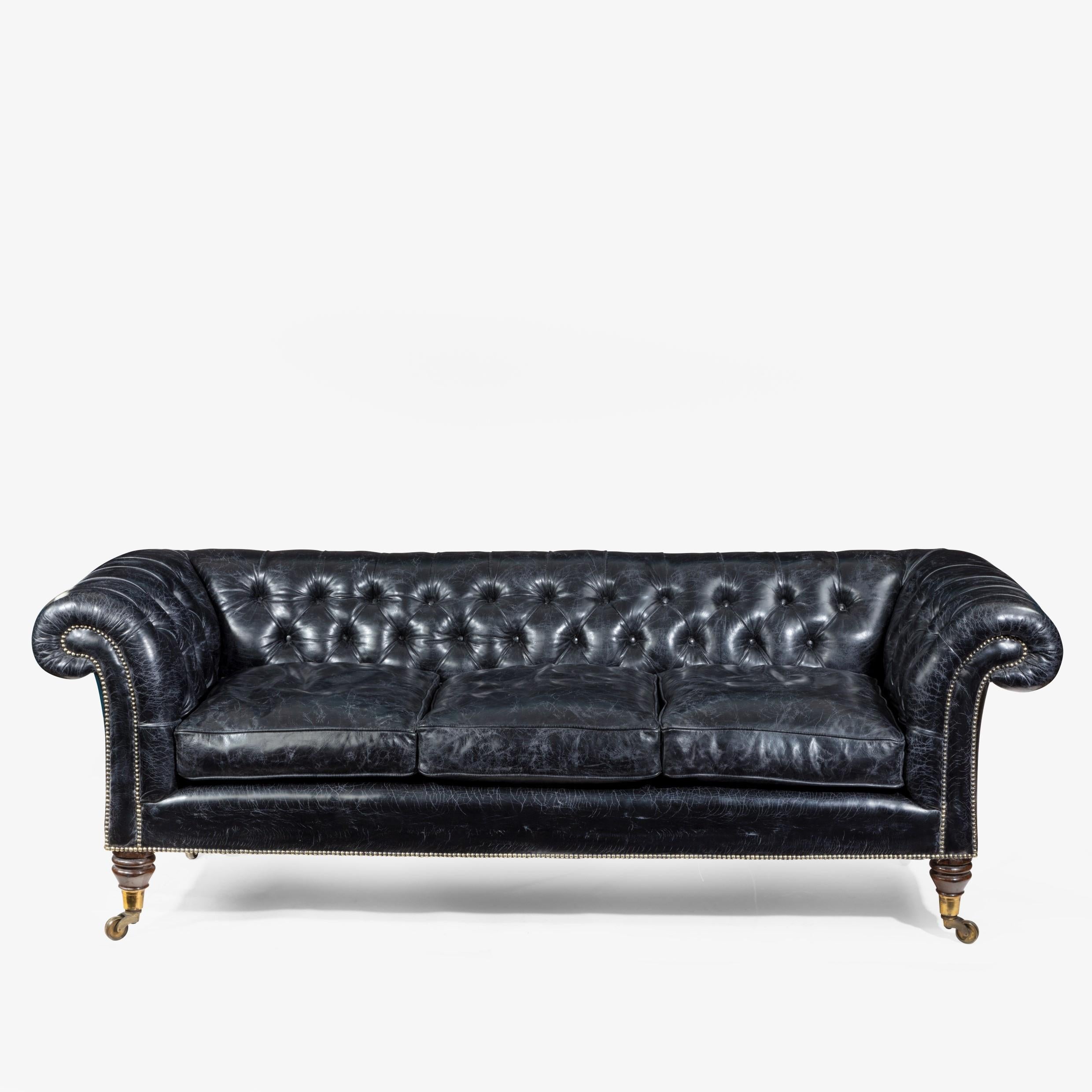 A late Regency country house three-seat sofa/Chesterfield, of typical form with rolled back and arms and turned flanged rosewood legs terminating in the original brass castors, fully re-upholstered in distressed buttoned black leather, English,