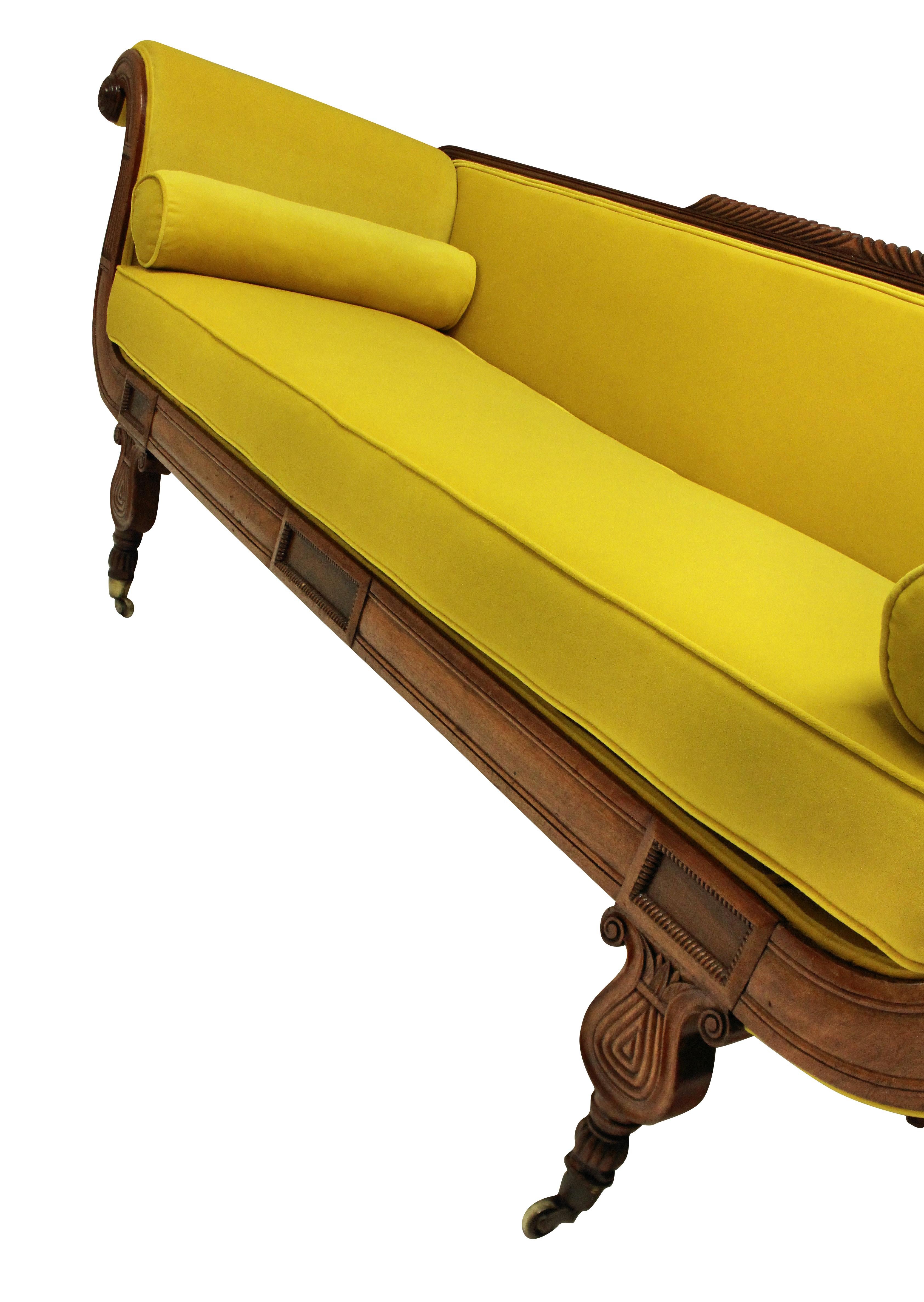 An English Regency daybed, of neoclassical design in crisply carved mahogany and newly upholstered in chartreuse velvet.