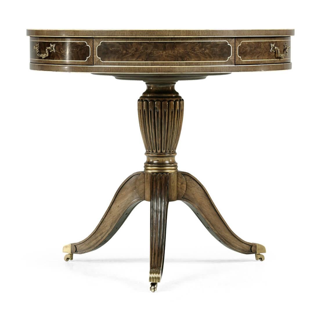 English Regency style bleached mahogany drum table with a tooled leather inset top, figured crotch mahogany-paneled cross banding with three frieze drawers each with brass handles above a reeded pedestal with three splay reeded legs raised on brass