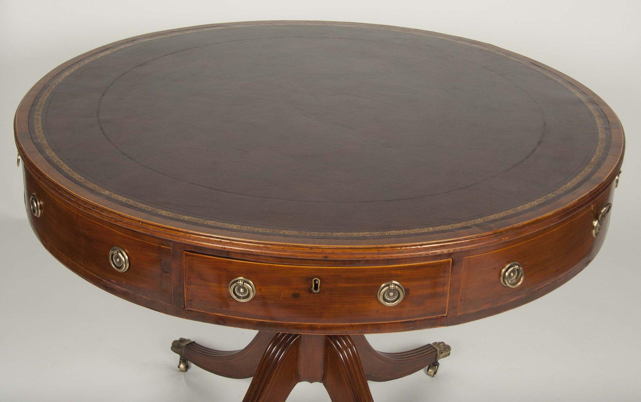 An English Regency mahogany revolving drum table with leather top, pencil inlays, four drawers, and raised on pedestal base with sabre legs on paw foot casters.