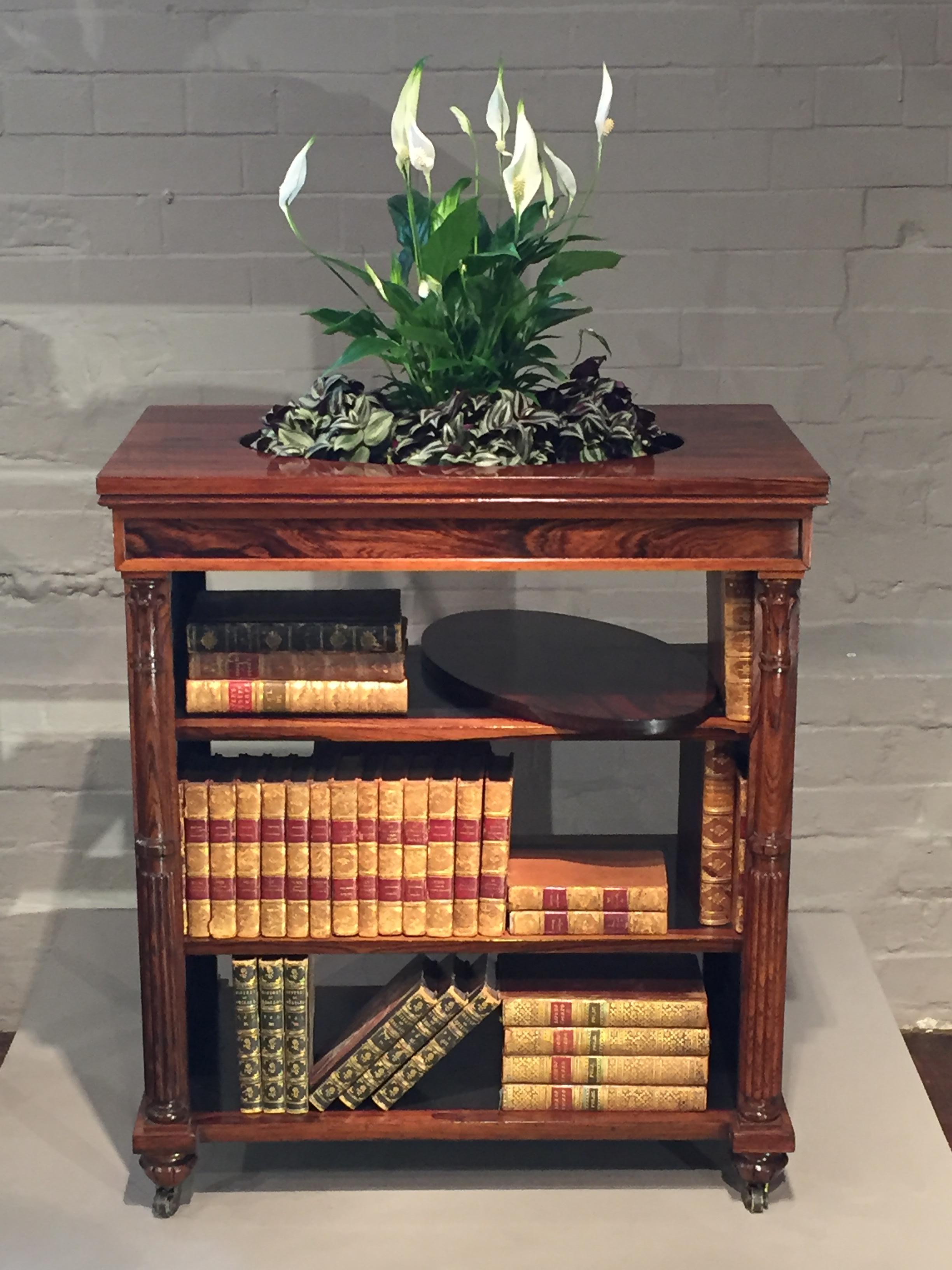 A charming, attractive and useful Regency period centre open bookcase jardinière.
The cabinet of finely figured rosewood with pleated silk panel ends, split classical column corners and a removable oval lid to the jardinière, on castors.
A most