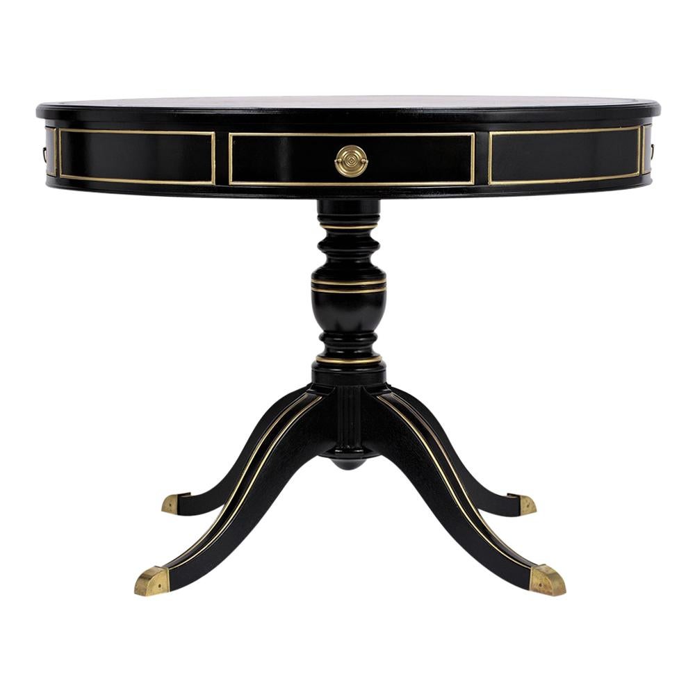 This Early 1900s Antique Regency Center Table comes with the original embossed leather top that has been newly dyed in a dark forest green color and features a new ebonized lacquered finish with gilt trim details. The tabletop comes with