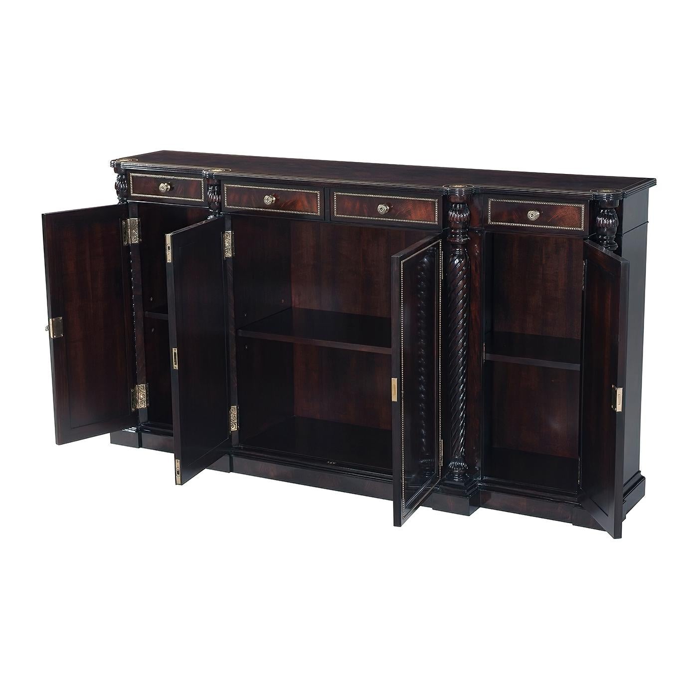 A Regency style ebonized flame mahogany buffet, the breakfront top with a reeded edge, brass stringing and brass inlaid rosettes above four paneled frieze drawers and four doors with brass beaded molding and engraved brass hinges, the doors
