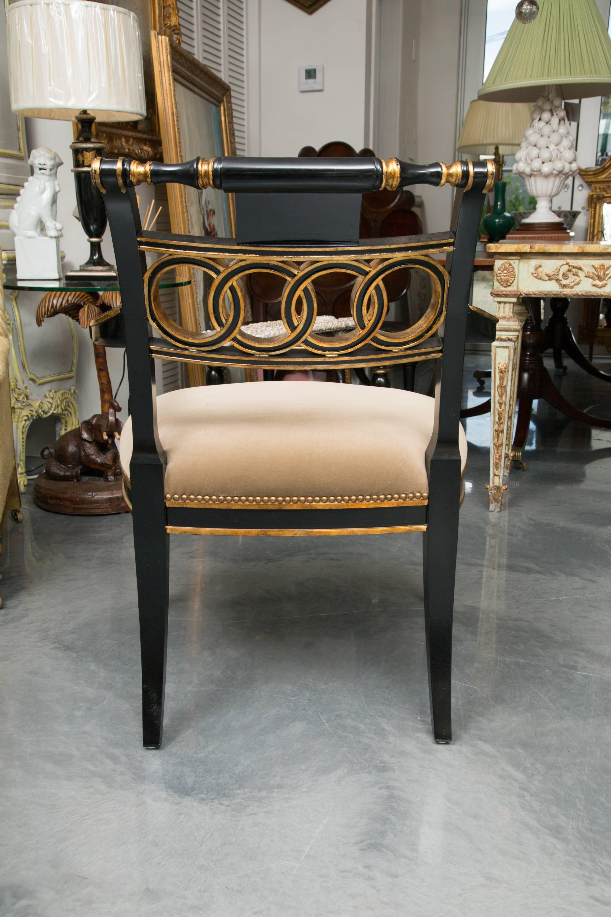 This is an elegant ebonized and parcel-gilt Regency style armchair with a top rail over a backsplat carved with concentric circles, flanked by gently curved arms above a padded seat and raised on faux bamboo carved legs, 20th century.