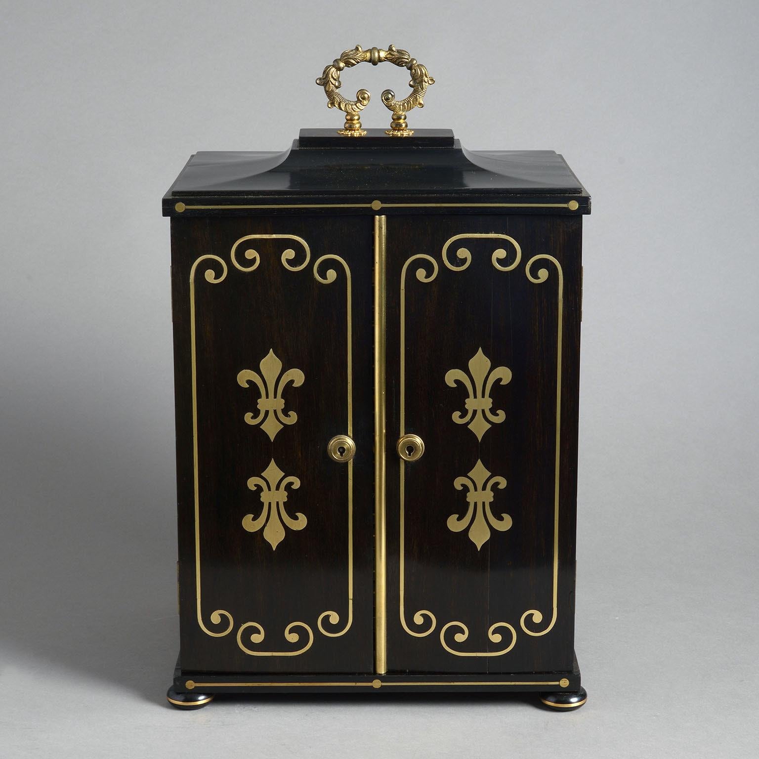 A regency ebony and brass inlaid collector’s cabinet constructed in a combination of solid ebony and veneered ebony over a mahogany substrate and decorated on all sides with brass inlay. 

The pair of doors with original Bramah lock opening to